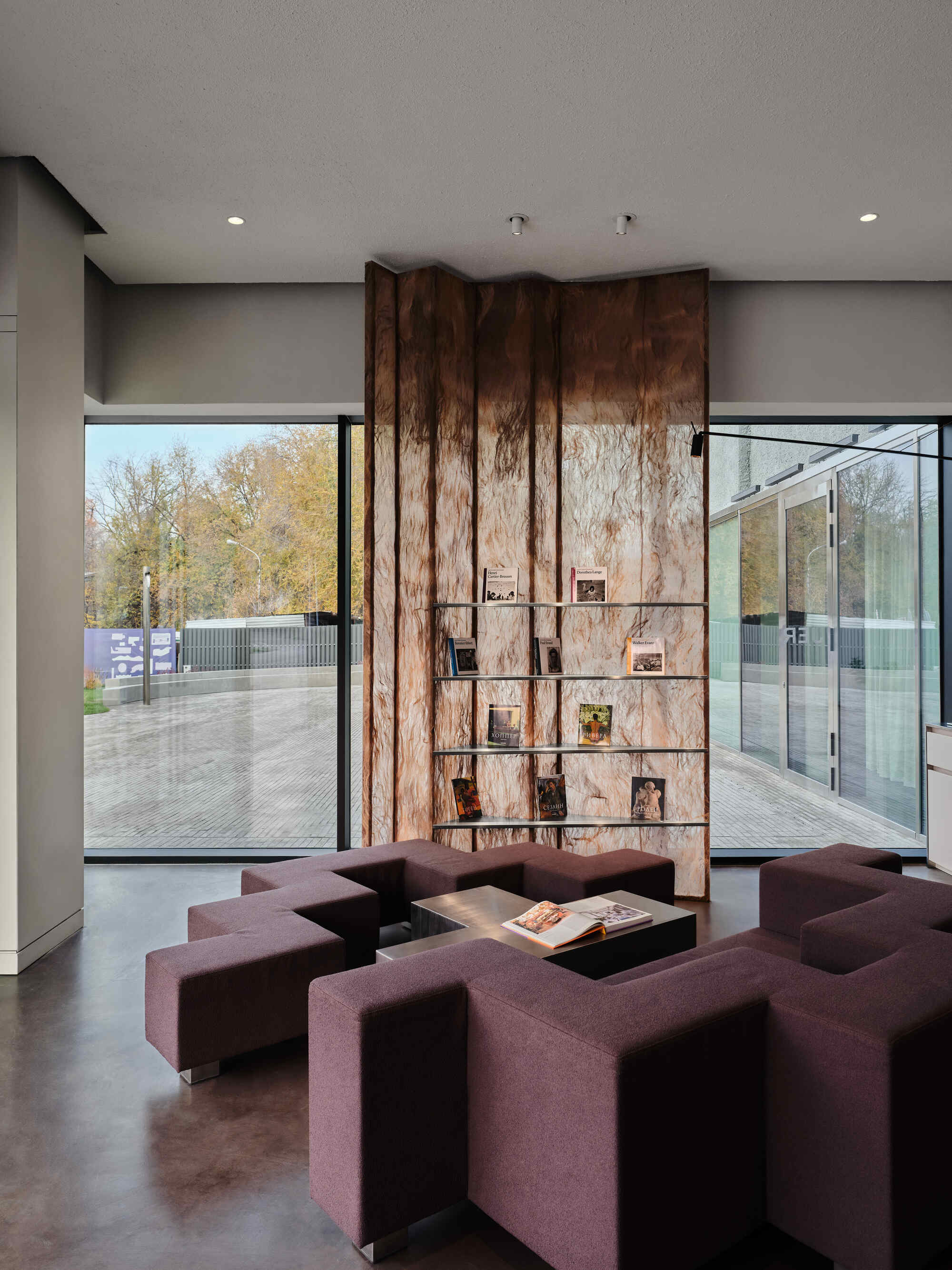 Tall timber wall panel with integrated display niches flanked by floor-to-ceiling windows framing autumn trees outside