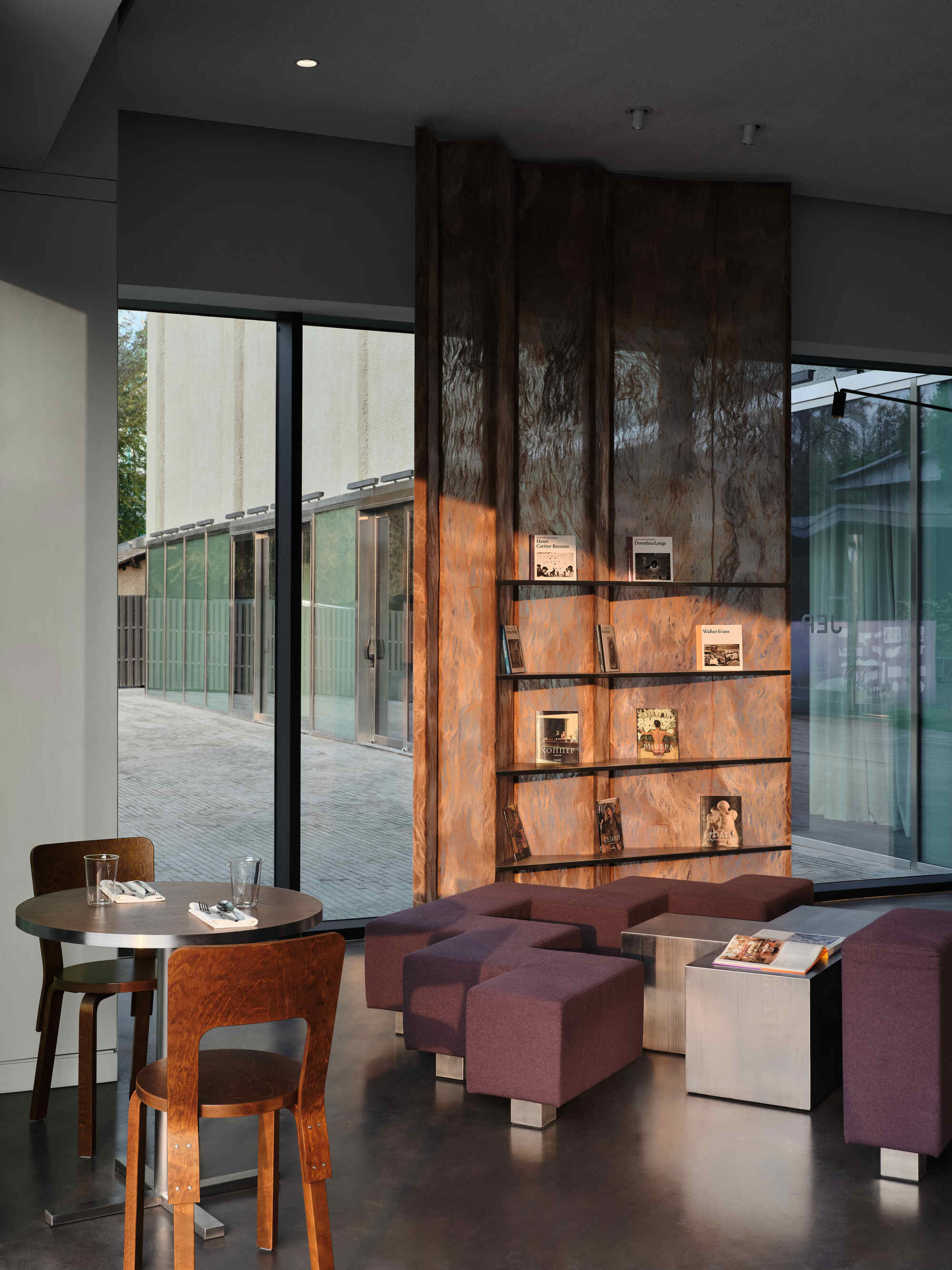 Backlit wood veneer display shelves with cutout animal silhouettes, overlooking a paved courtyard through glass doors