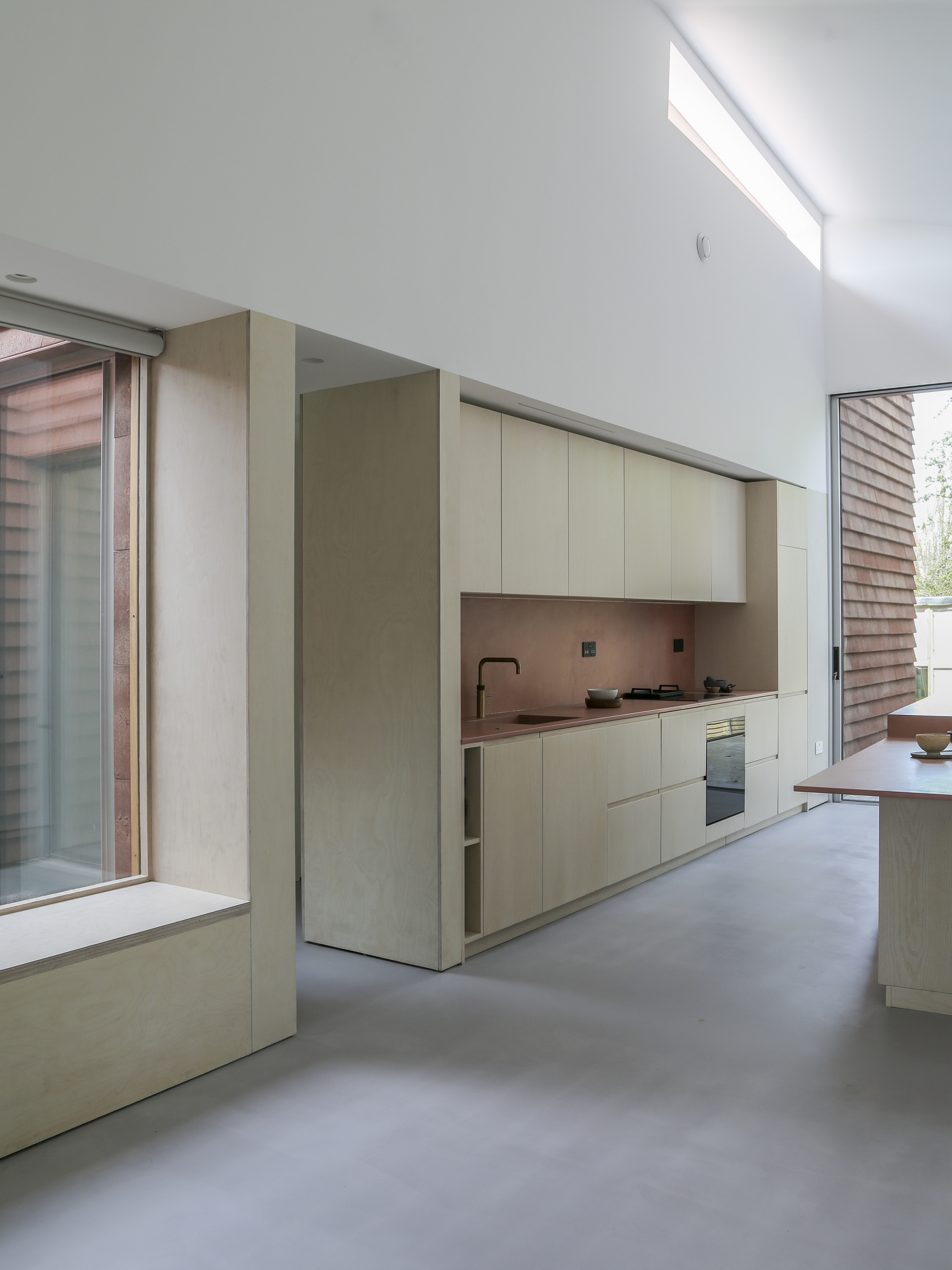 Kitchen with pale timber cabinetry and polished concrete floor beneath sloped ceiling with clerestory glazing