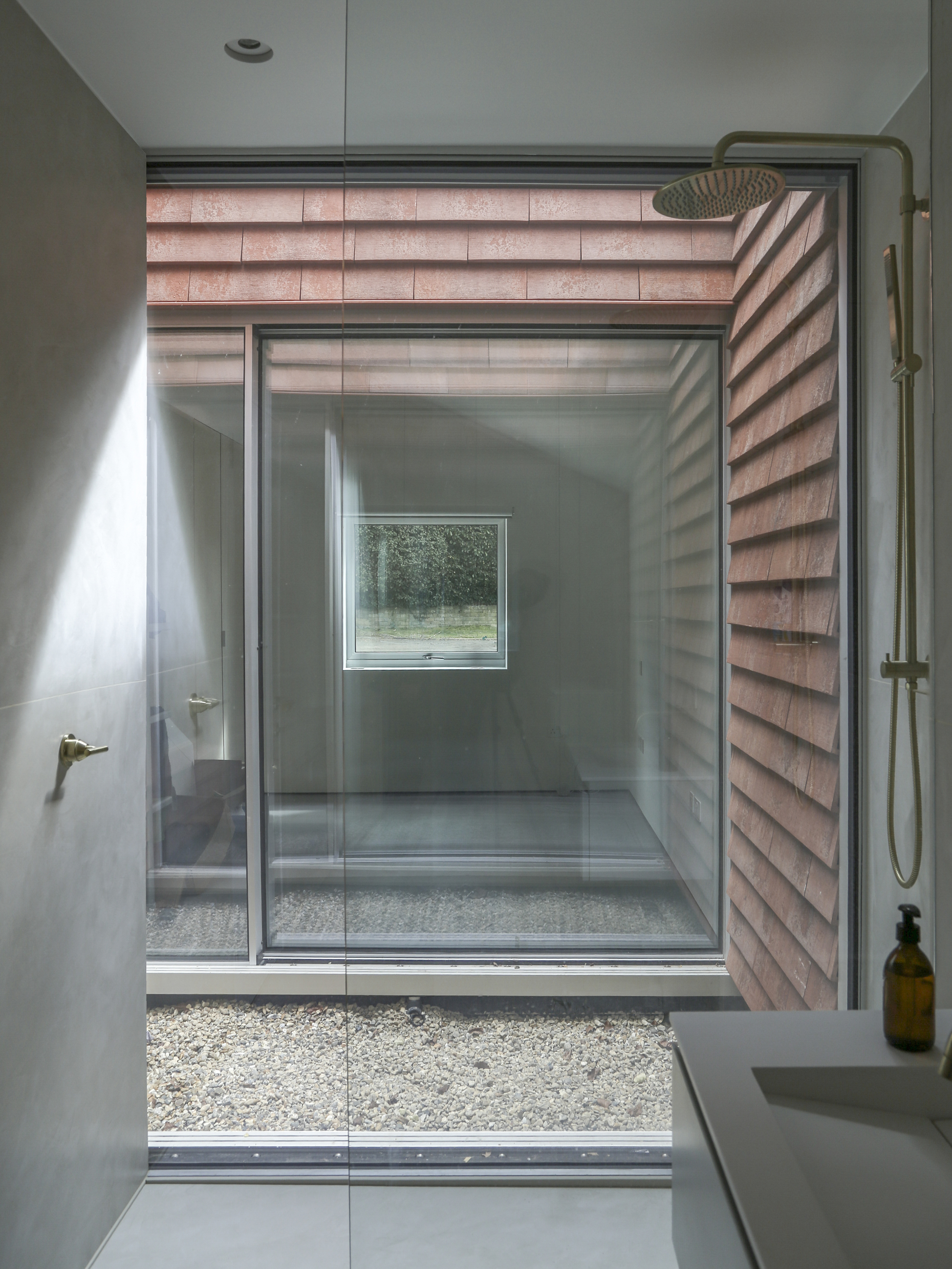 Bathroom with glass-enclosed shower opening to gravel courtyard framed by terracotta tile walls