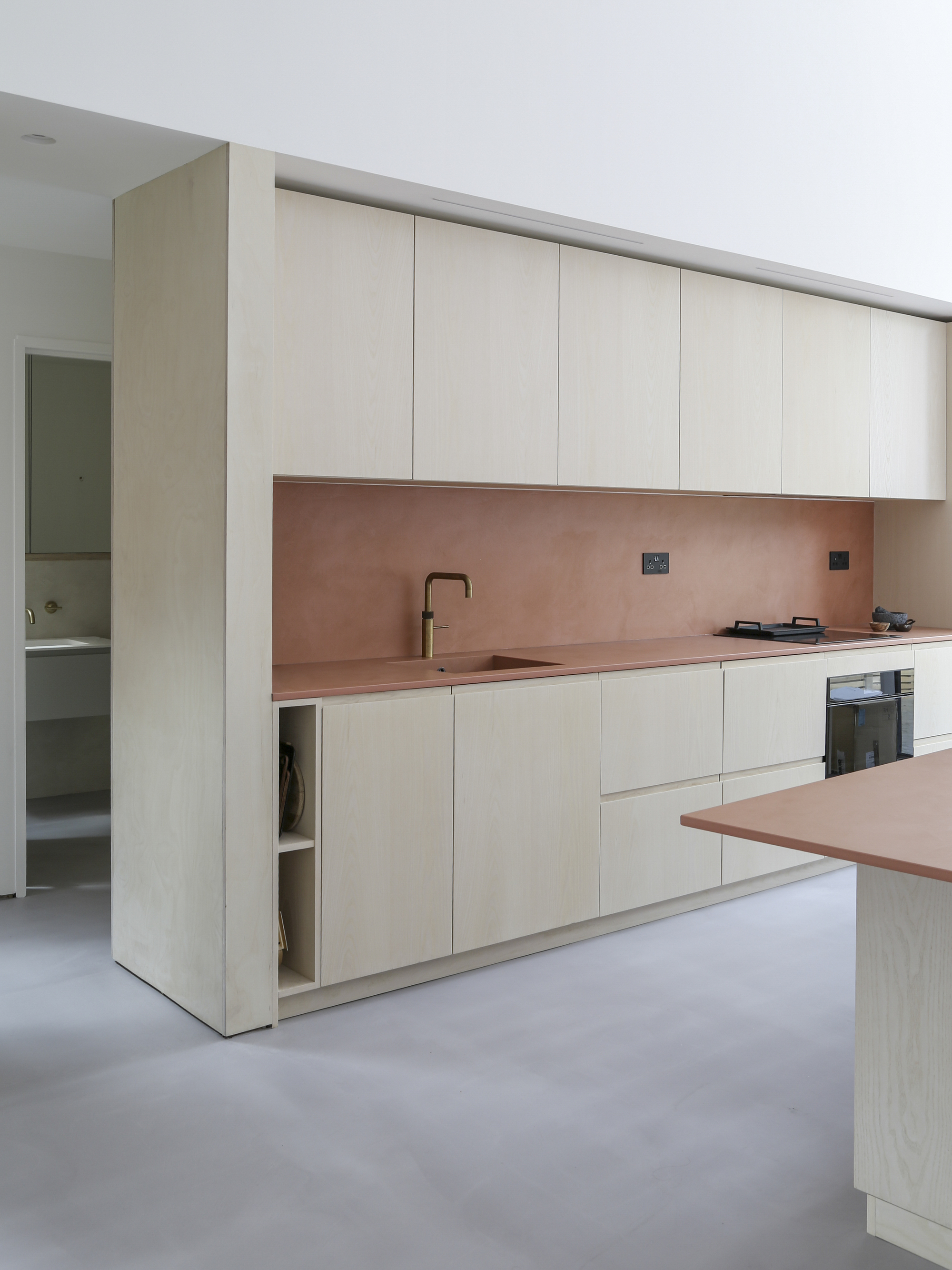 Kitchen wall with pale timber cabinets and copper-toned splashback and countertop on polished concrete floor
