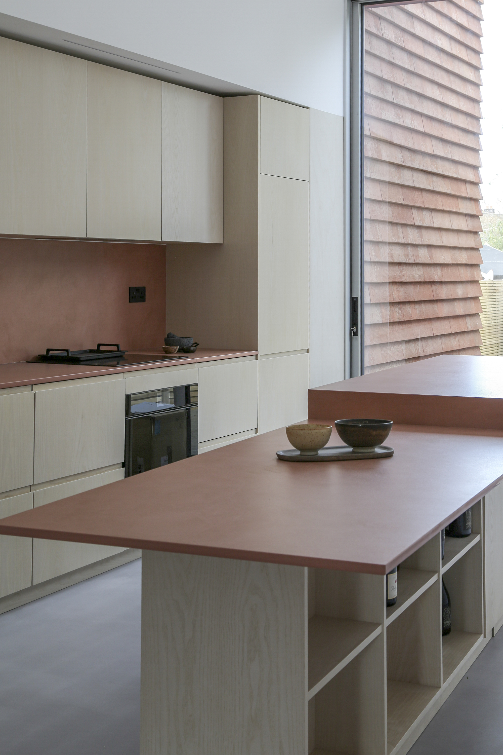 Kitchen island with copper countertop facing glazed door and timber-clad exterior wall