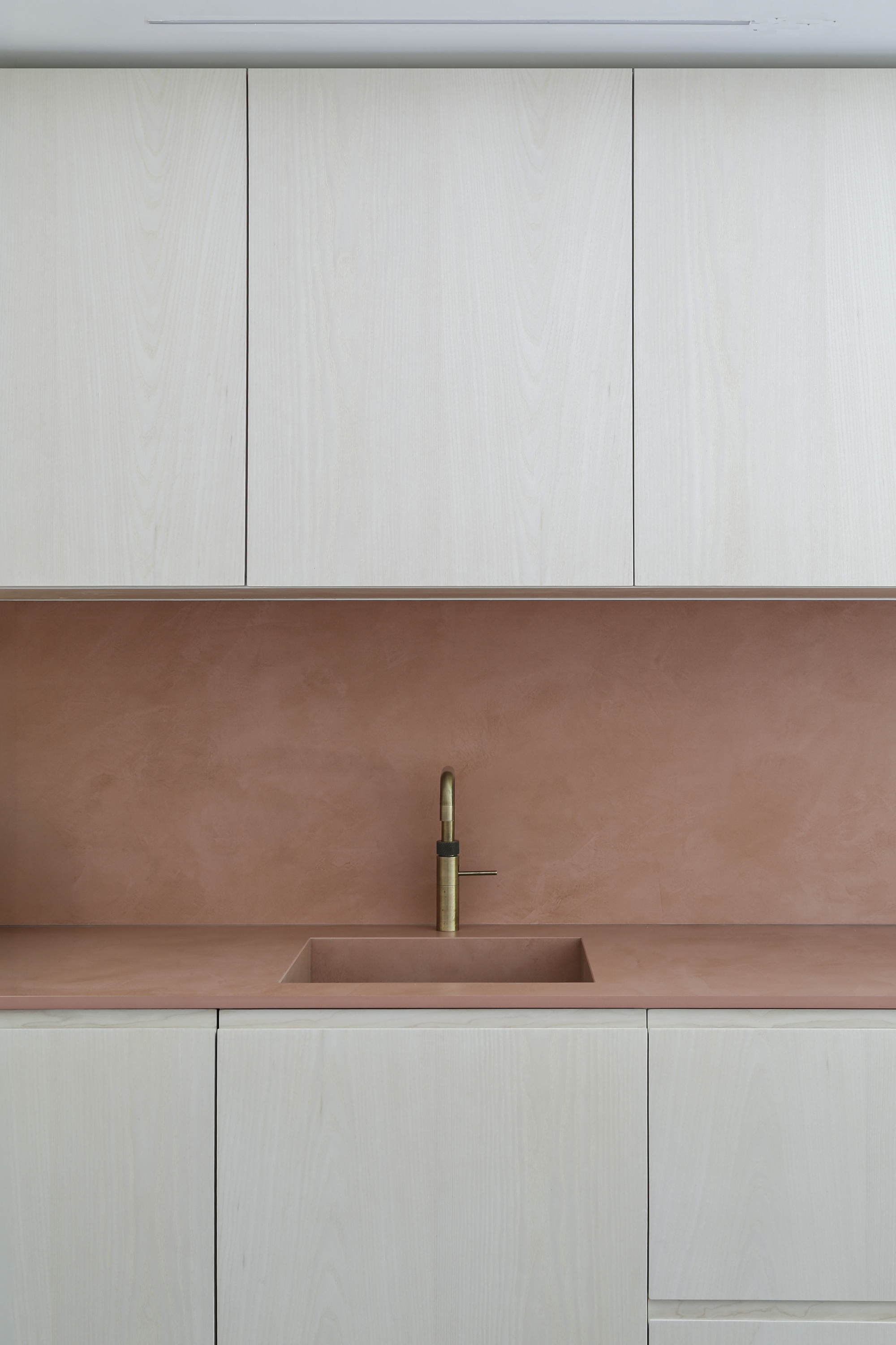 Close-up of copper sink and brass tap set into matching countertop beneath pale timber upper cabinets