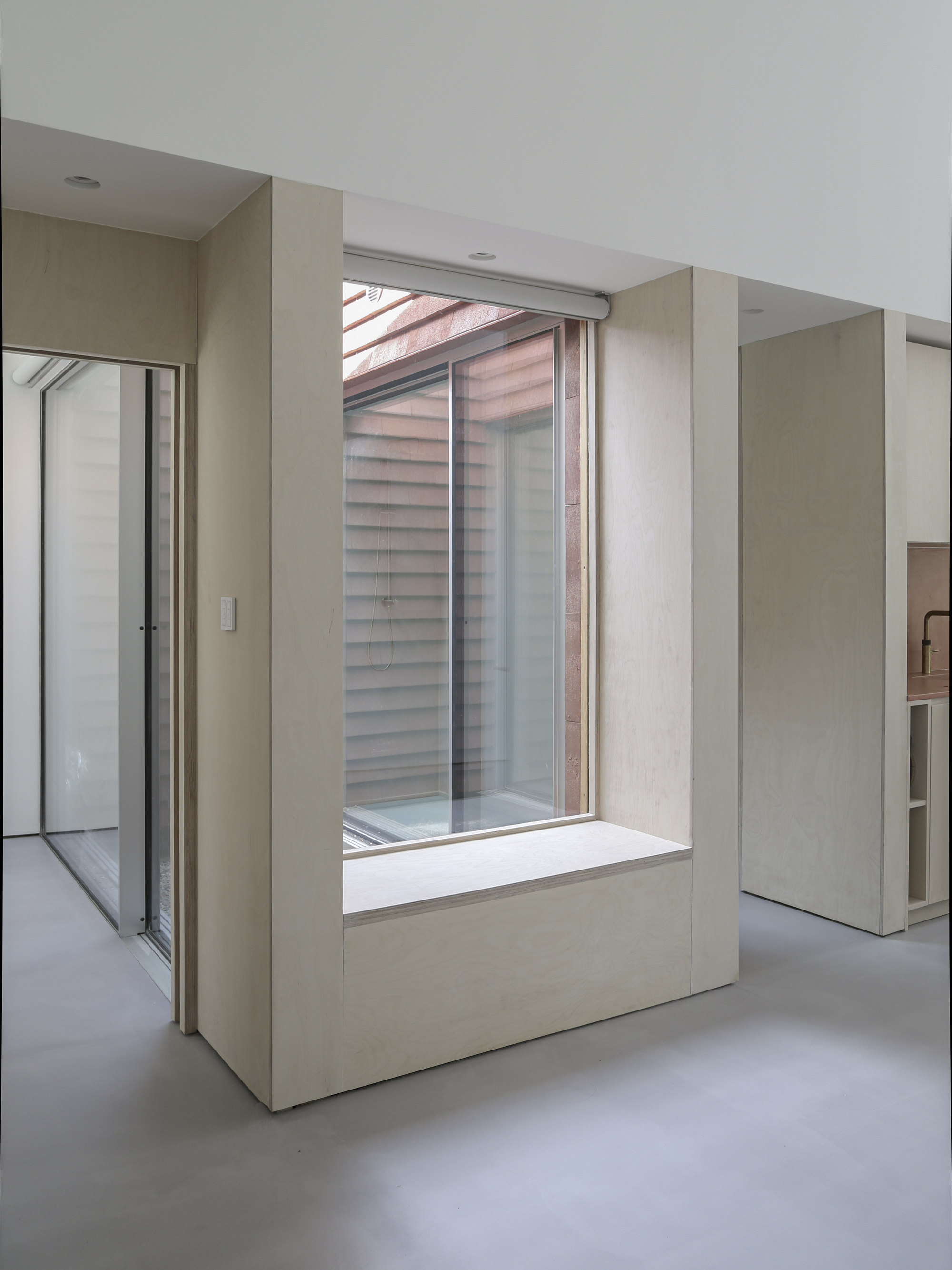 Built-in window seat framed by pale timber panels looking onto timber-slat screened courtyard