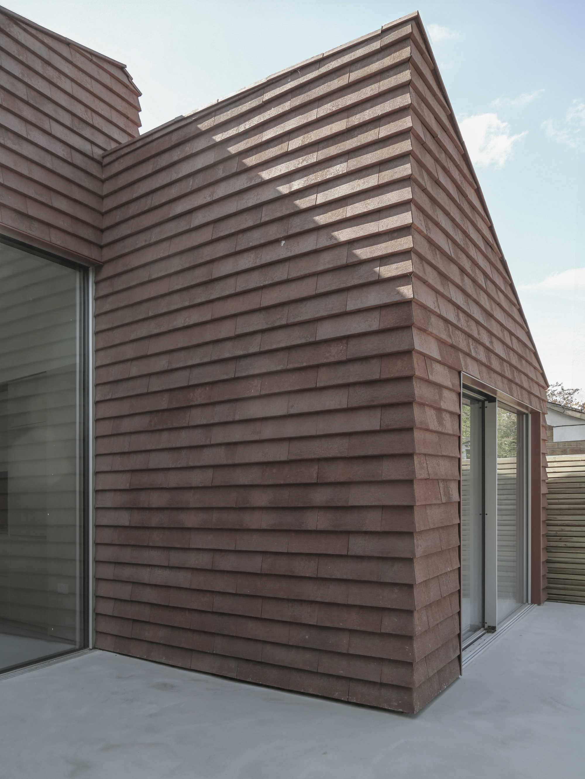 Angular timber-clad facade with glazed corner window under a clear blue sky