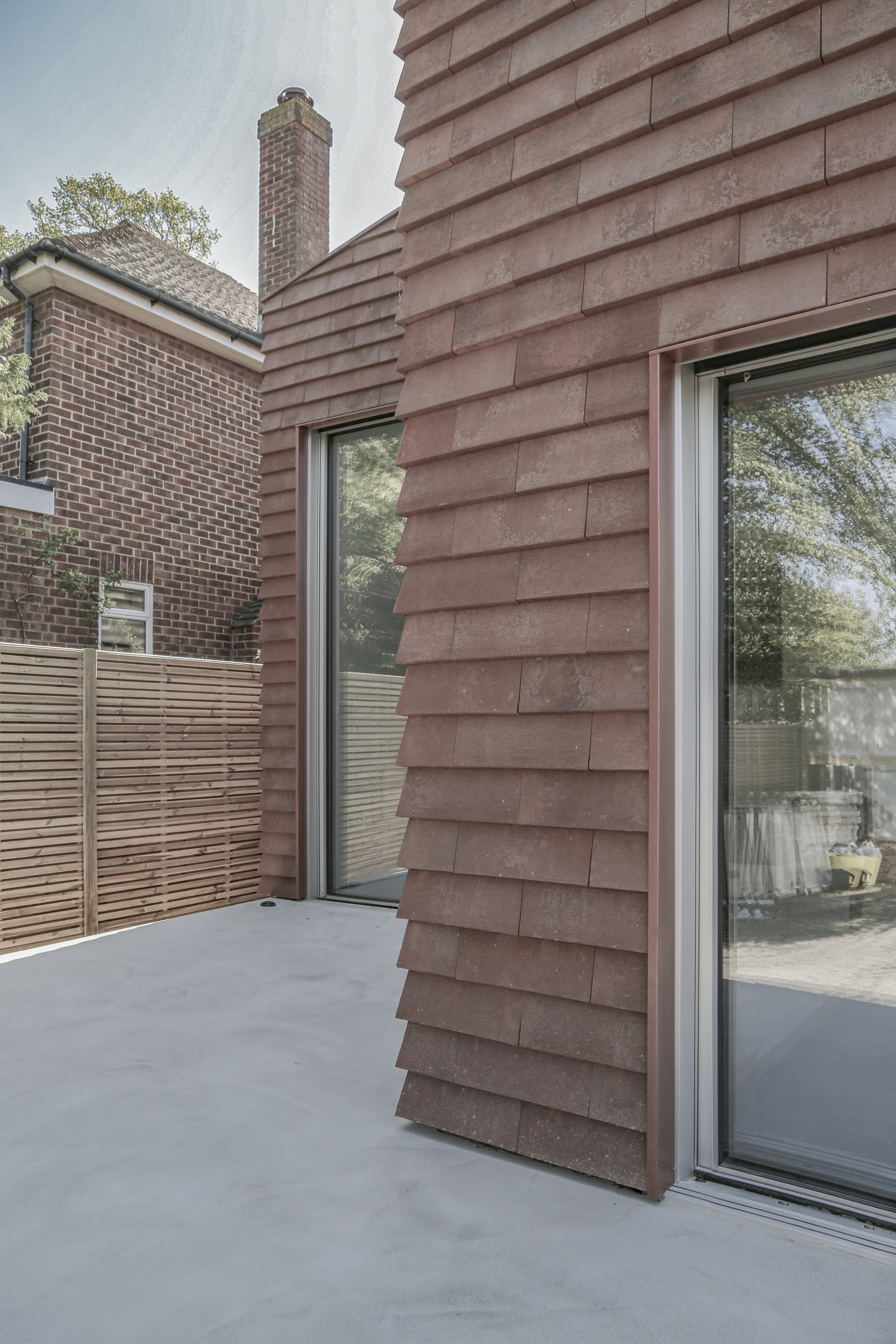 Sloped timber-shingled wall with flush-mounted glazing and timber fence in the background