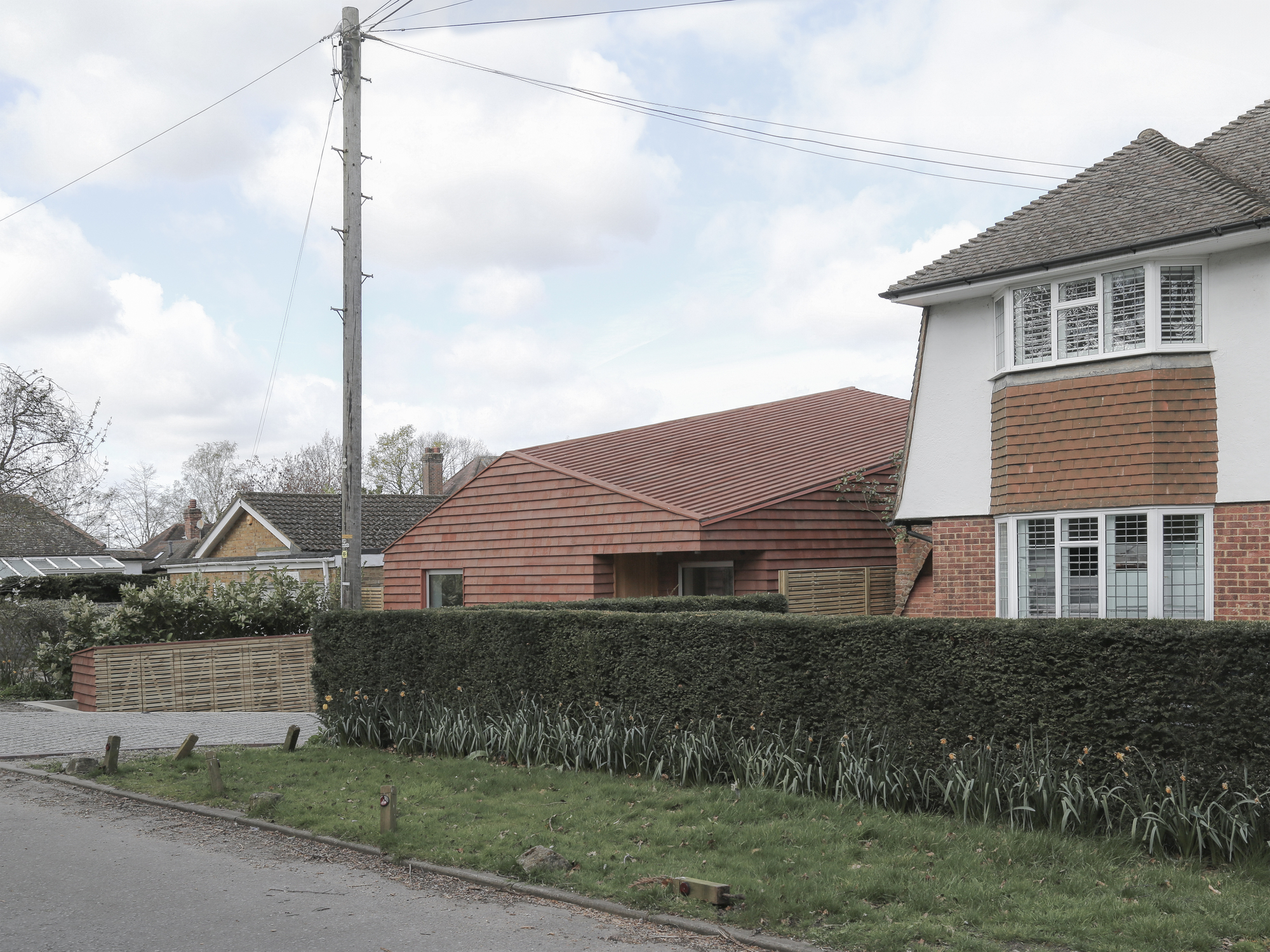 Street view of low-pitched tile roof extension beside brick houses on an overcast day