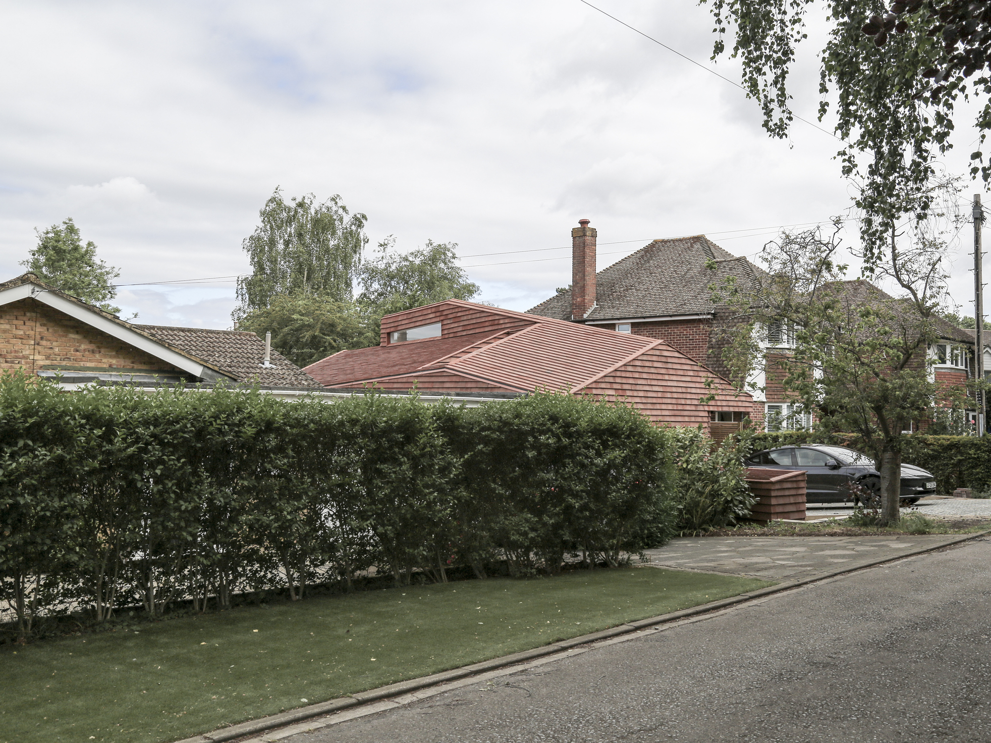 Street view of the ridged terracotta tile extension beside a trimmed hedge and neighboring brick houses