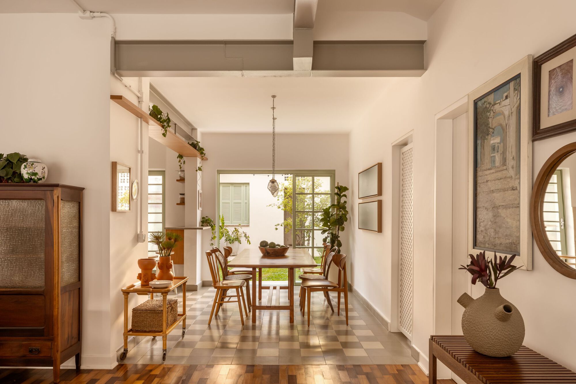 Corridor view through dining area to courtyard door framed by potted plants and checkered floor