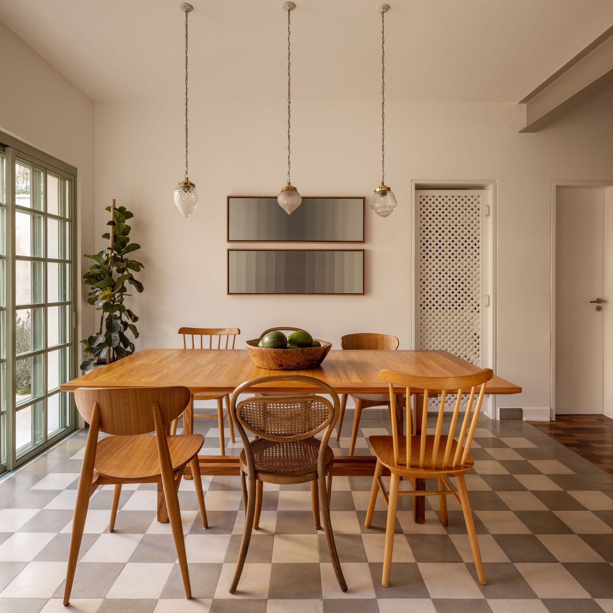 Dining room with timber table, mixed chairs, and lattice screen door under three glass pendant lights