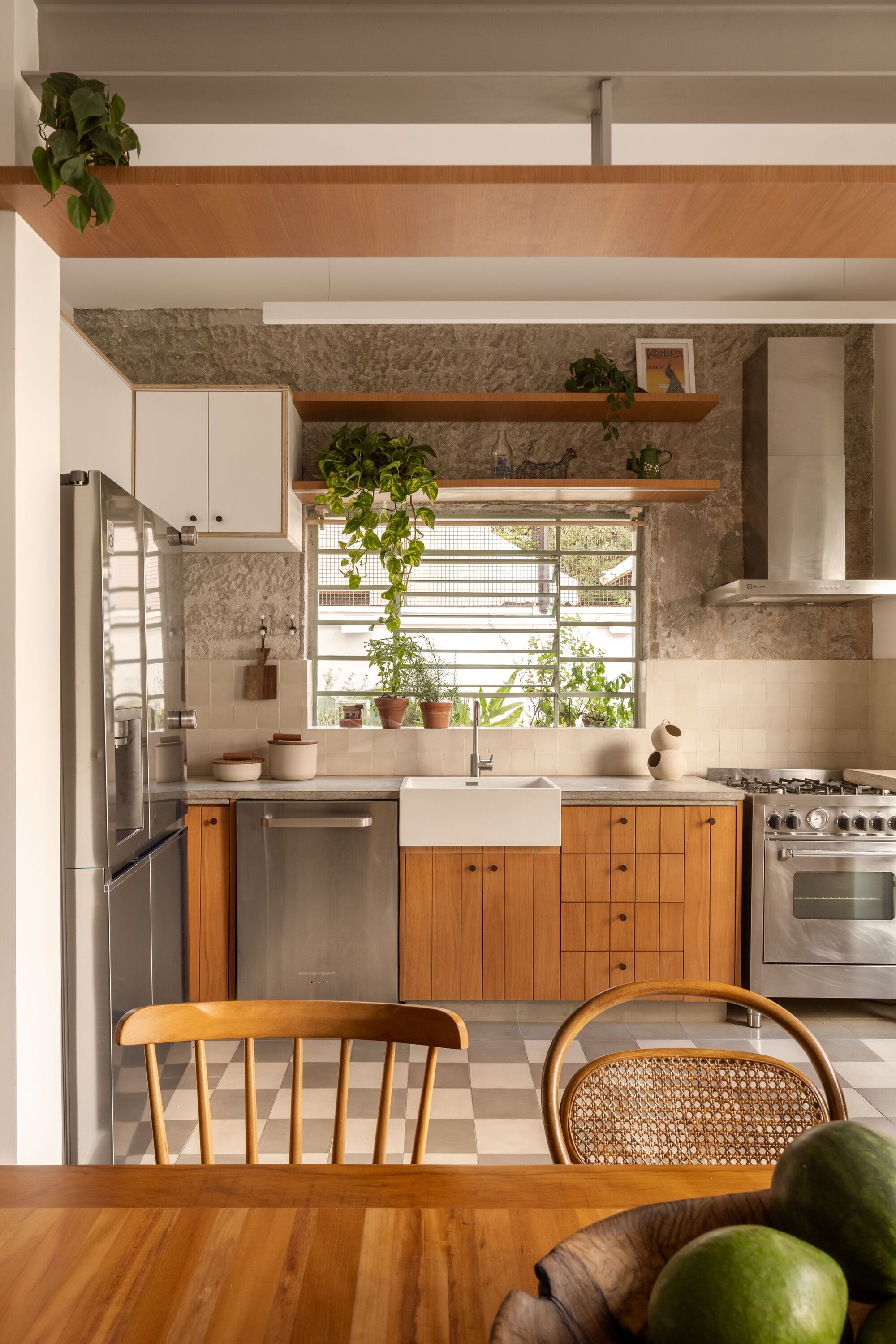 Kitchen counter with timber cabinetry, white farmhouse sink, exposed stone wall, and potted plants on the windowsill
