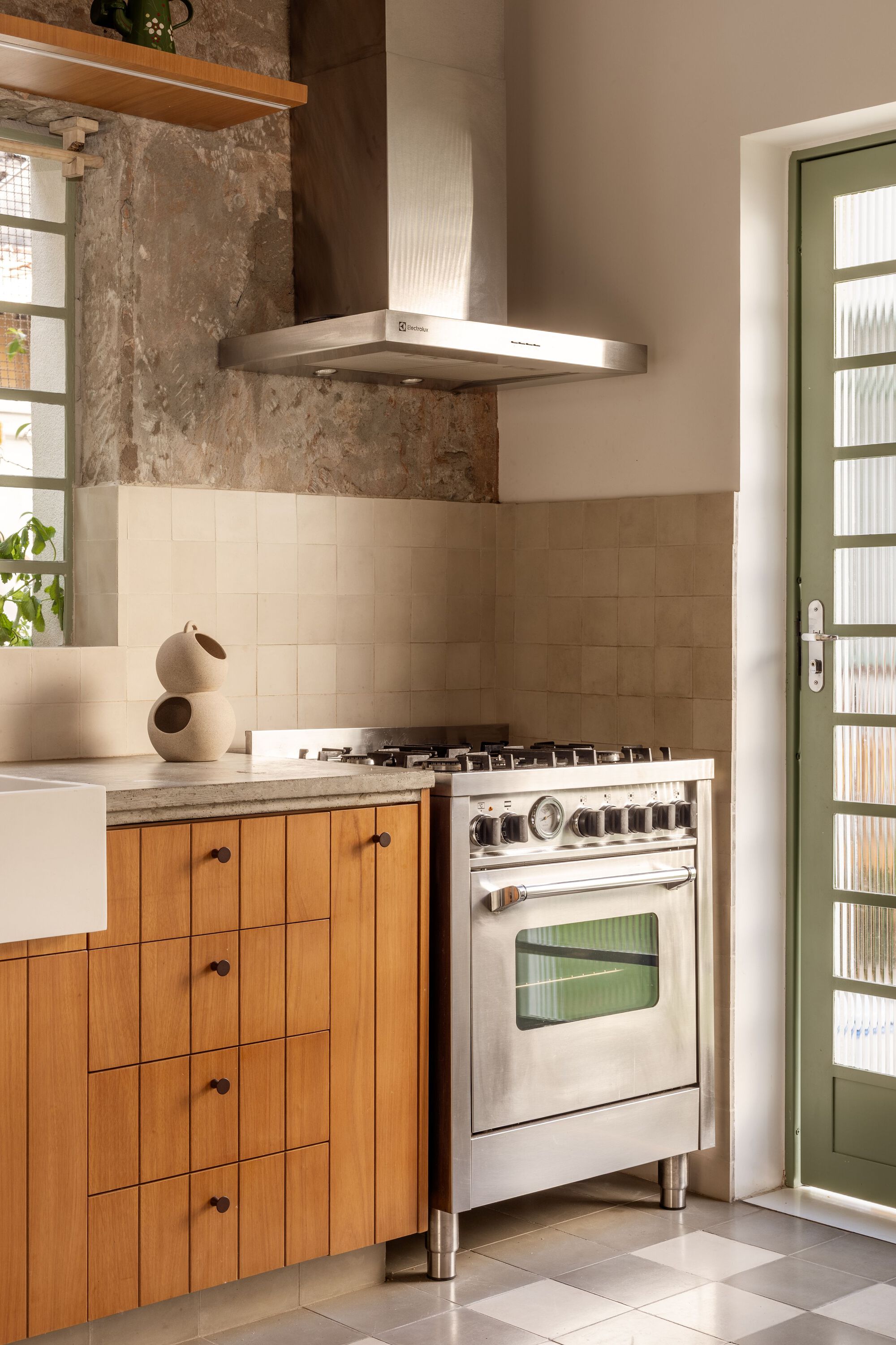Kitchen cooking zone with freestanding range, stainless hood, timber base cabinets, and exposed weathered wall above