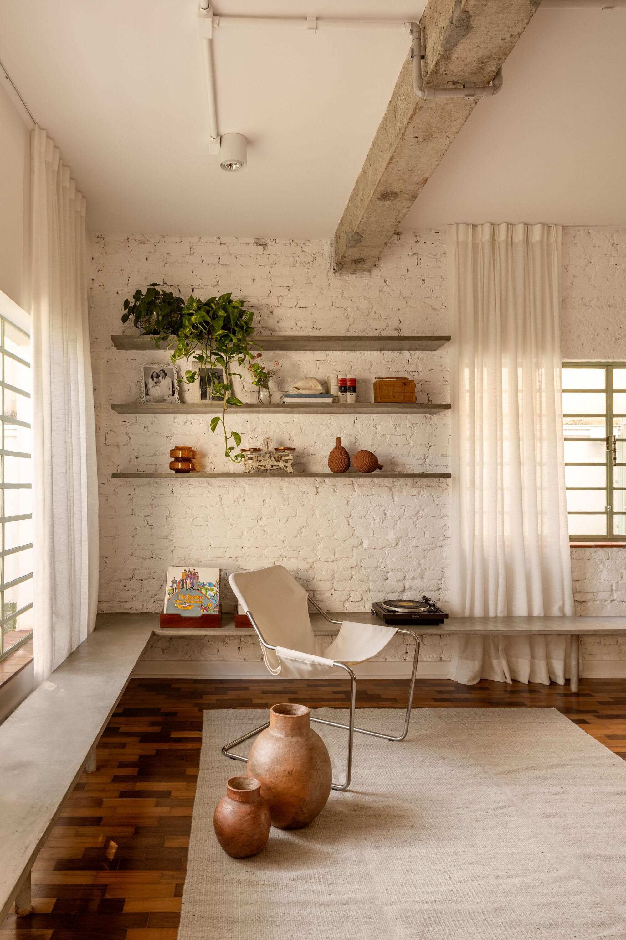 Living nook with white brick wall, floating shelves, exposed beam, parquet wood flooring, and sheer curtain divider