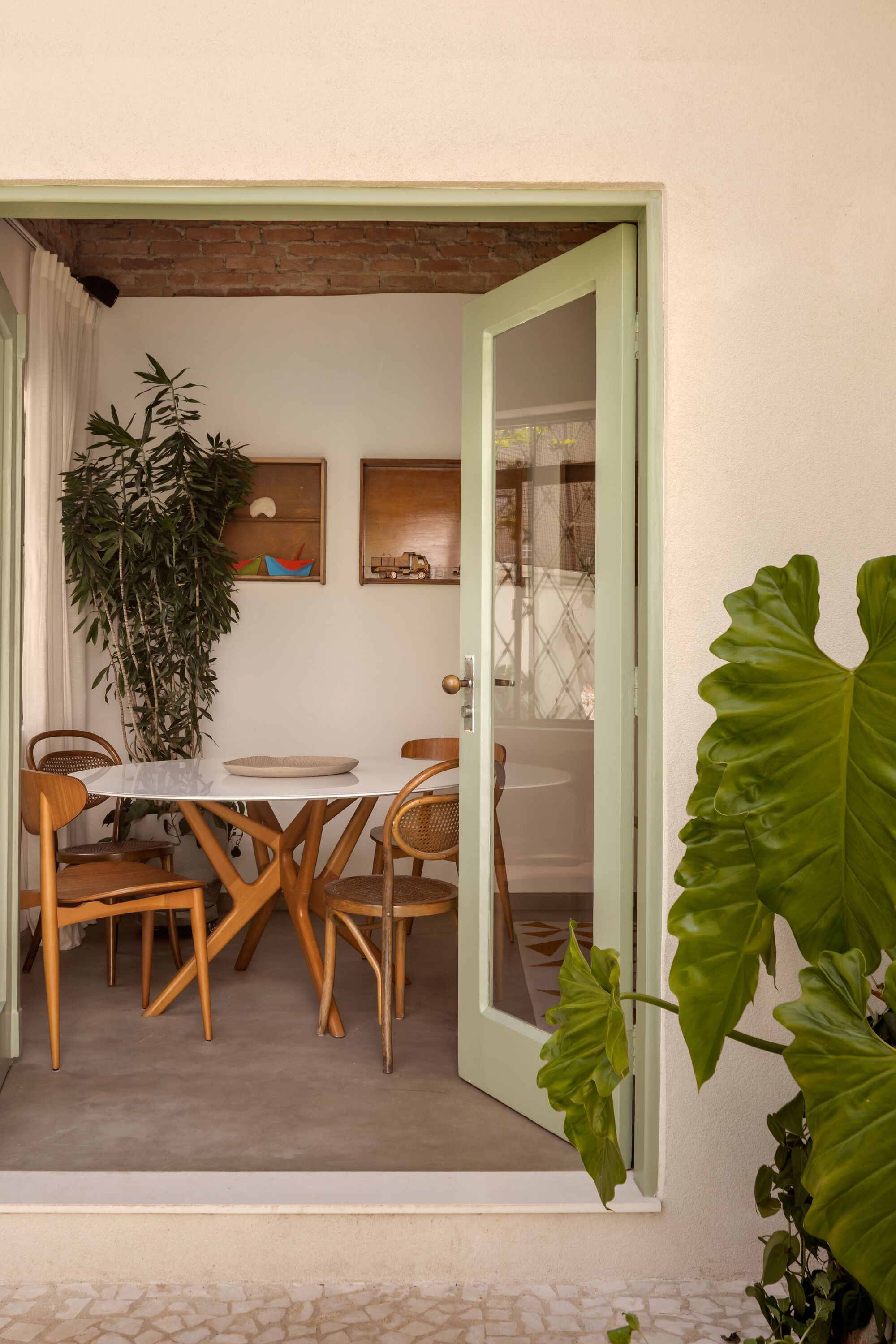Pale green door frame opening to dining area with exposed brick ceiling and large tropical plants