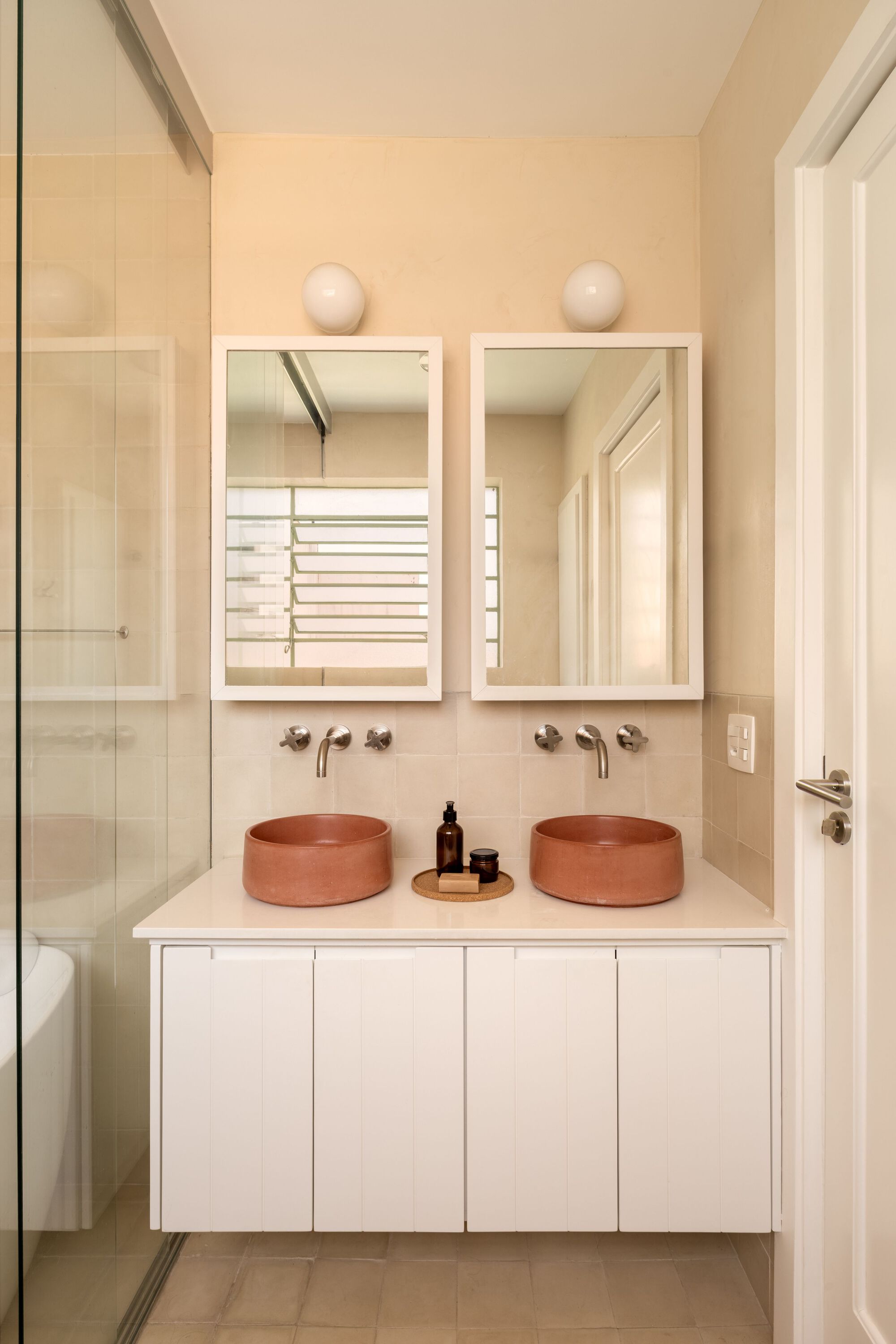 Double vanity with terracotta vessel sinks and white framed mirrors reflecting louvered shutters