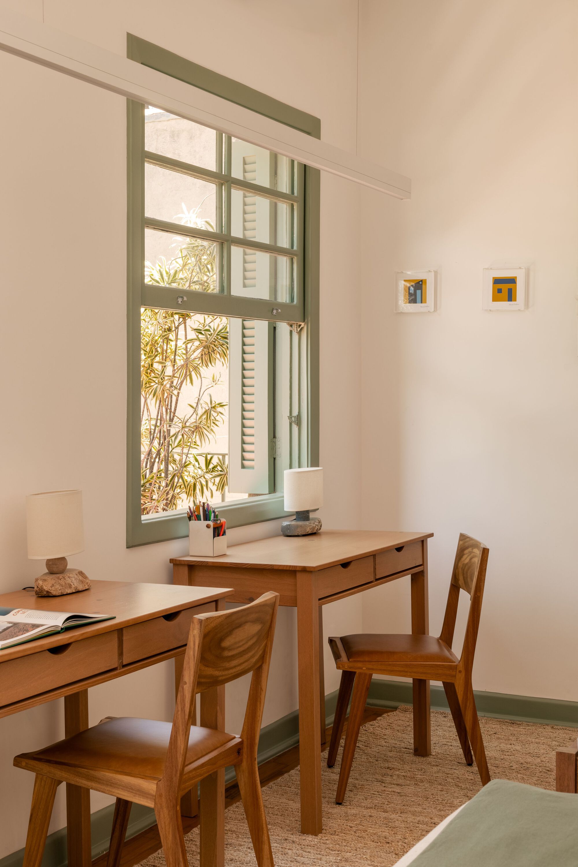 Study corner with wooden desks and chairs beneath tall window framing bamboo foliage outside