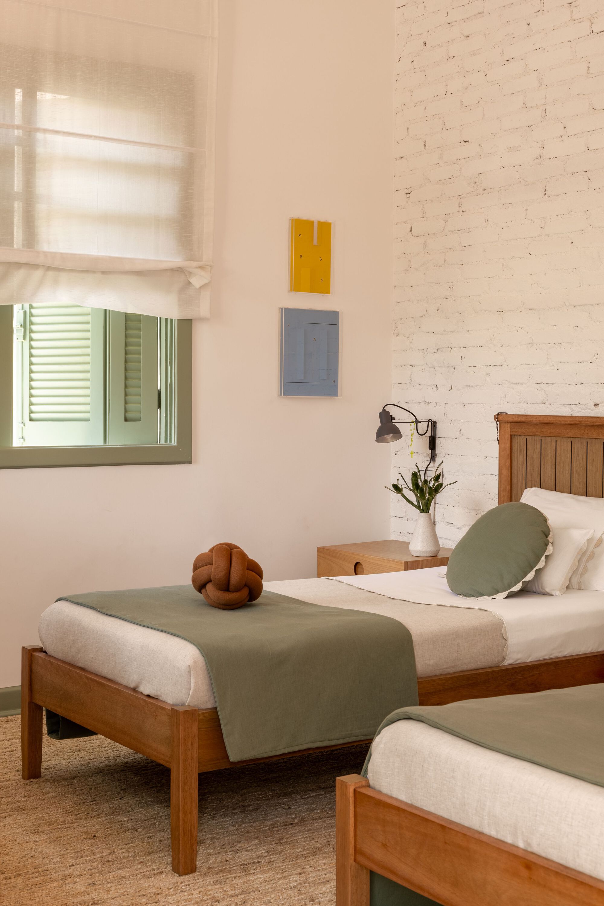 Twin beds with sage green runners beneath whitewashed brick wall and window with Roman shade