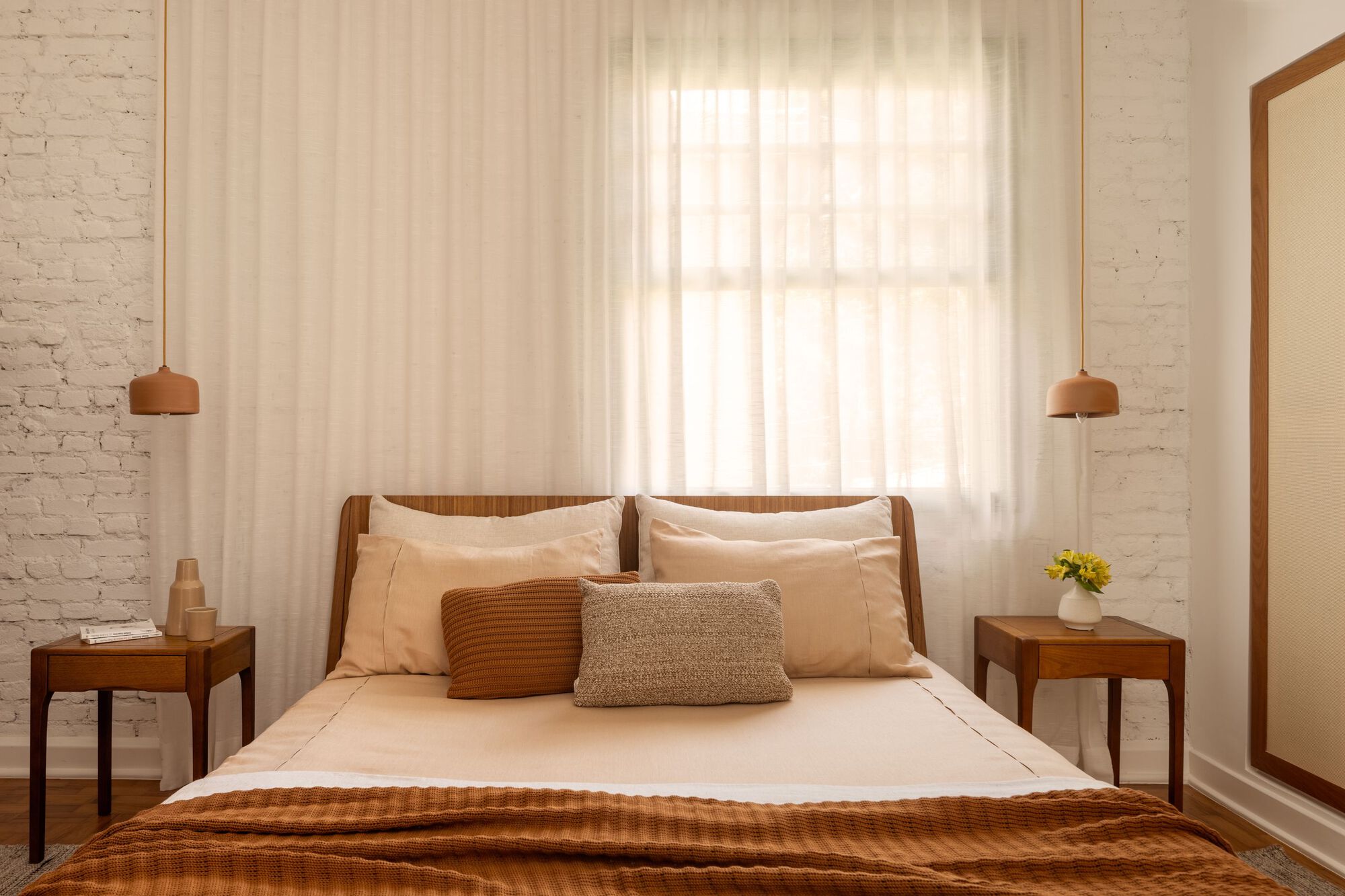 Bedroom with white brick wall, wooden bed frame and sheer curtains filtering afternoon light