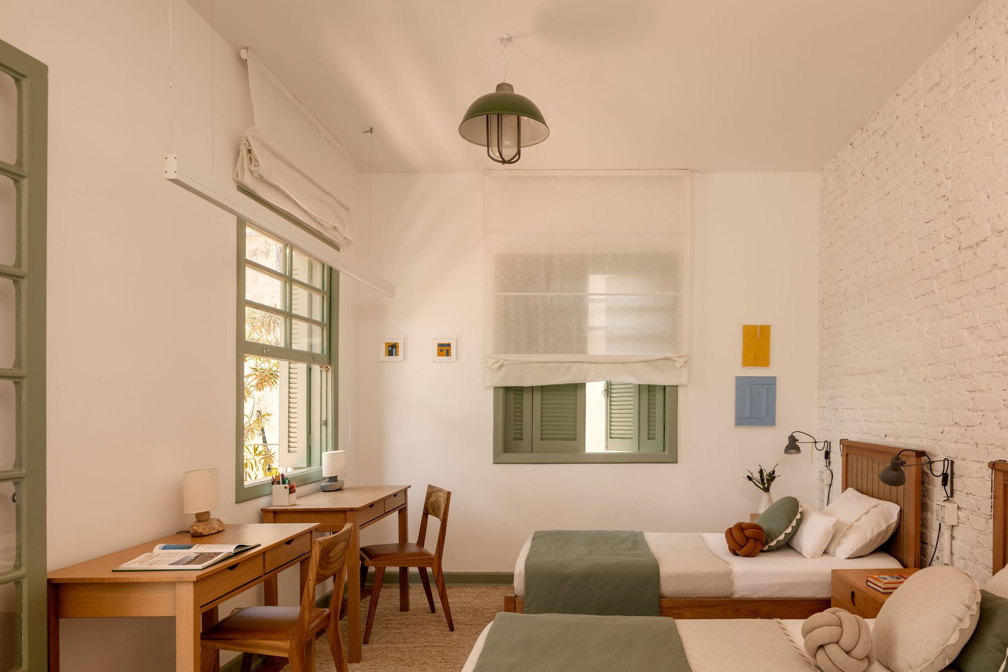 Twin bedroom with white vaulted ceiling, green-framed windows and timber work desk along the wall