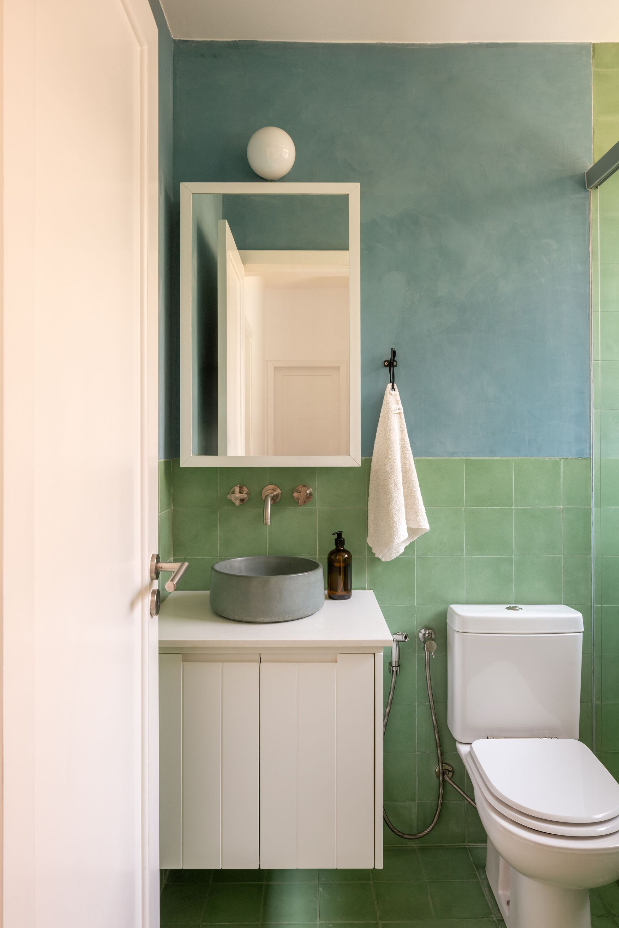 Compact bathroom with green tile wainscot, blue painted upper wall and white floating vanity