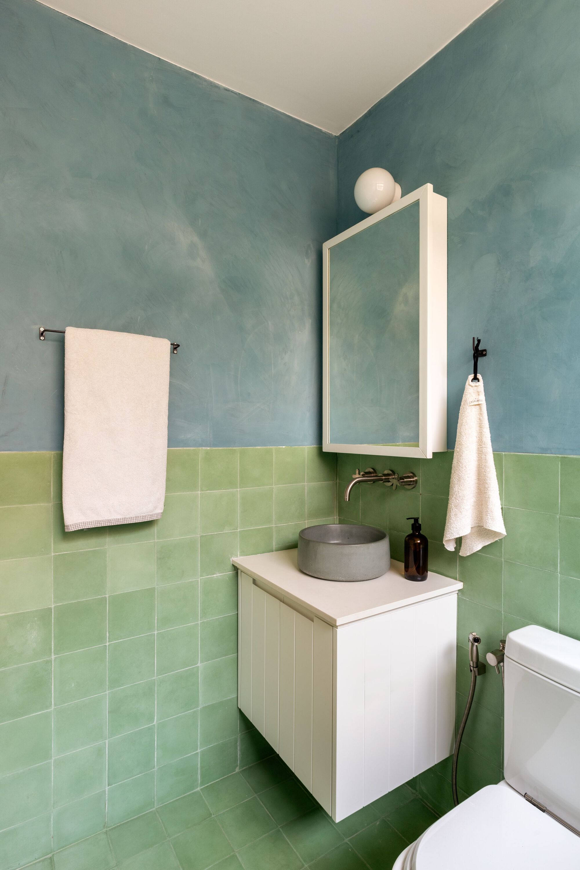 Corner bathroom with green square tile wainscoting beneath blue polished plaster walls