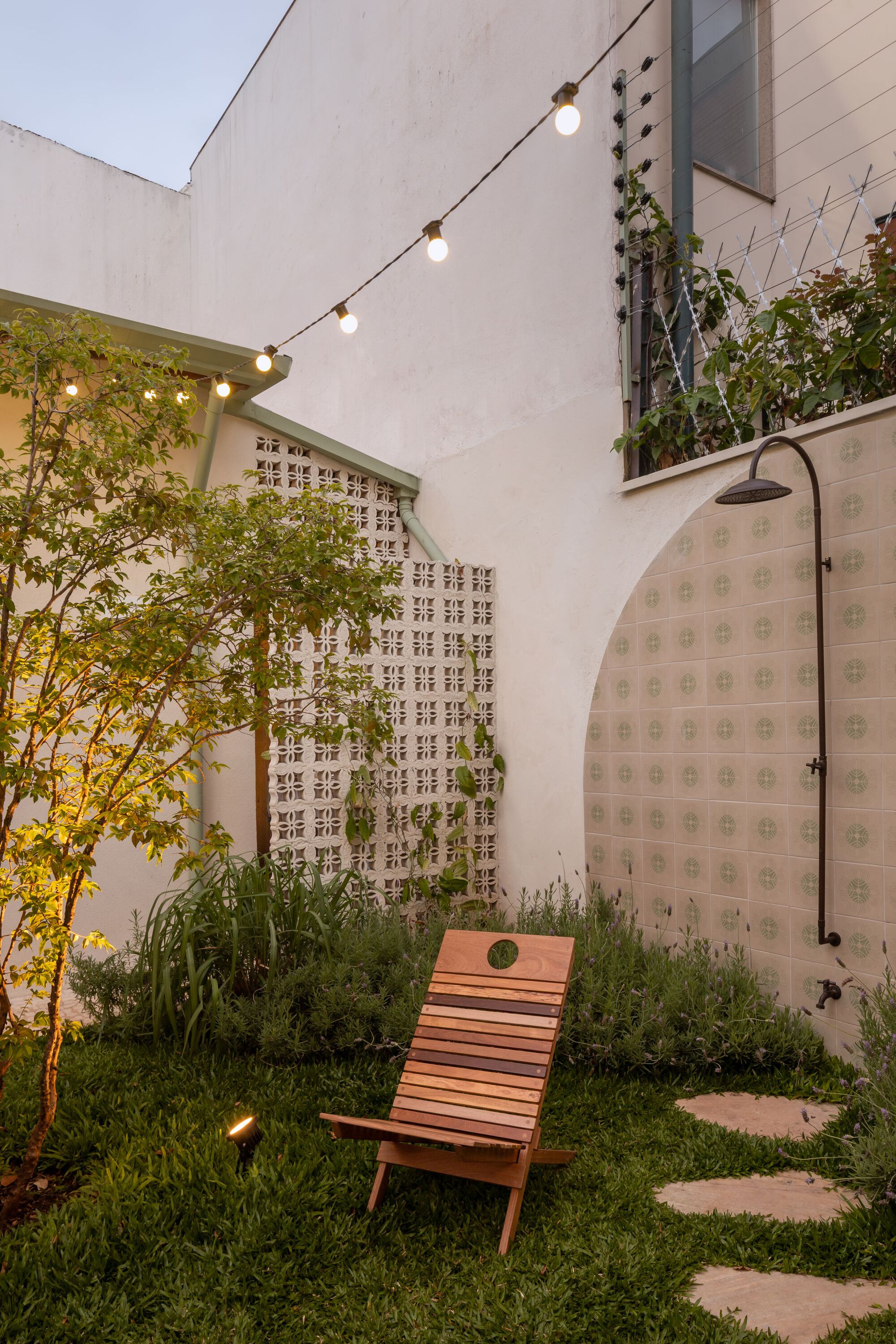 Courtyard garden with timber lounge chair beneath string lights and decorative breeze block wall