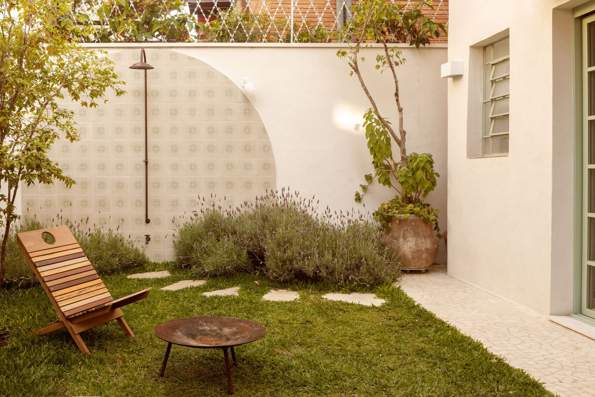 Walled courtyard with lavender beds, patterned tile shower and overhead timber lattice at golden hour