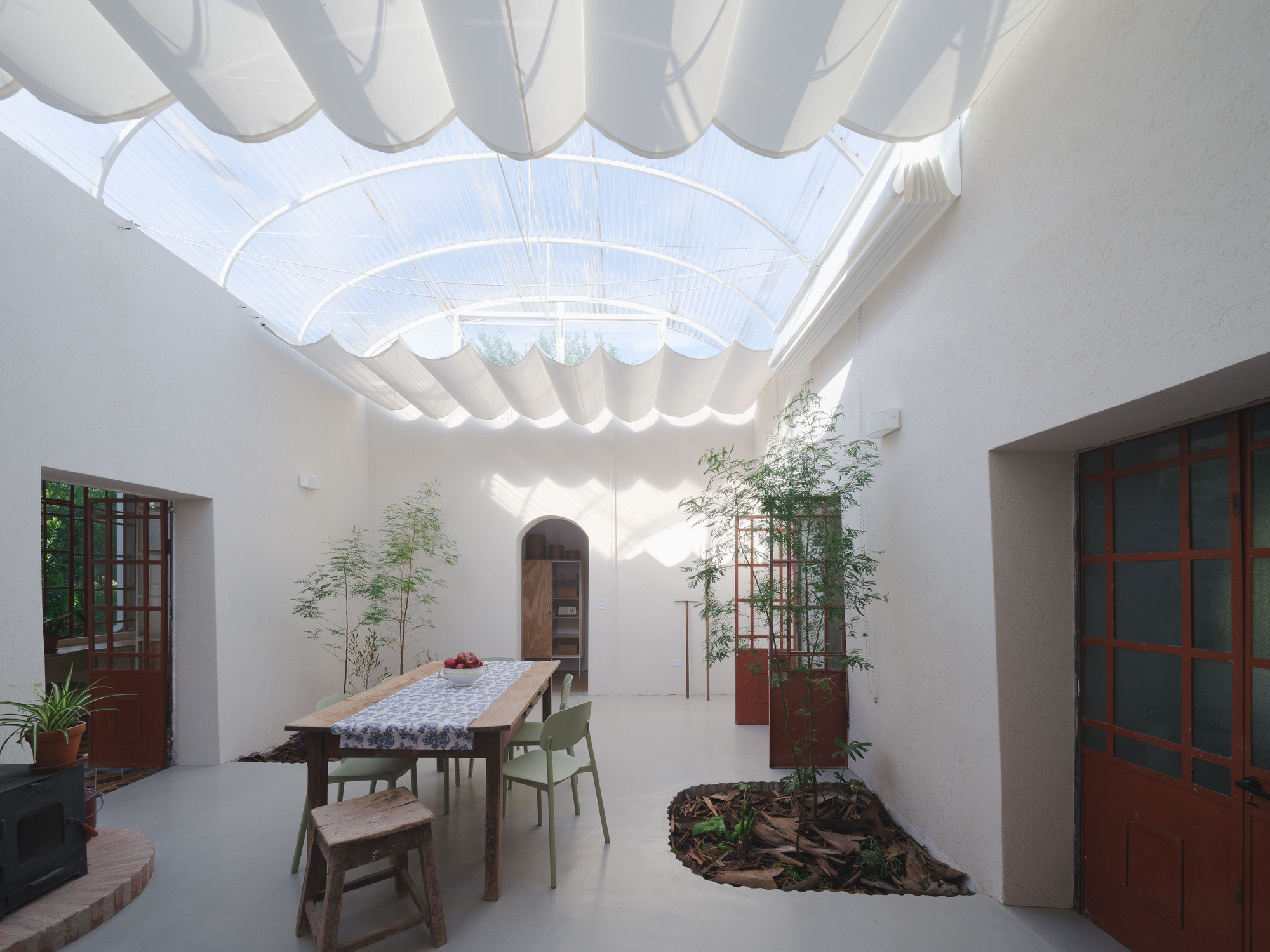 Interior courtyard with translucent corrugated canopy casting wave-like shadows on white walls and dining table