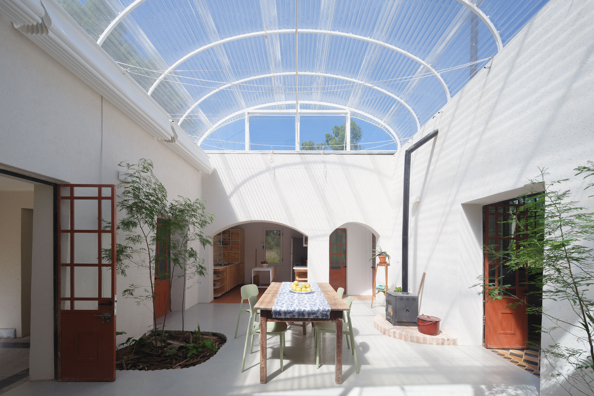 Courtyard with arched openings and translucent corrugated roof flooding white walls with dappled midday light