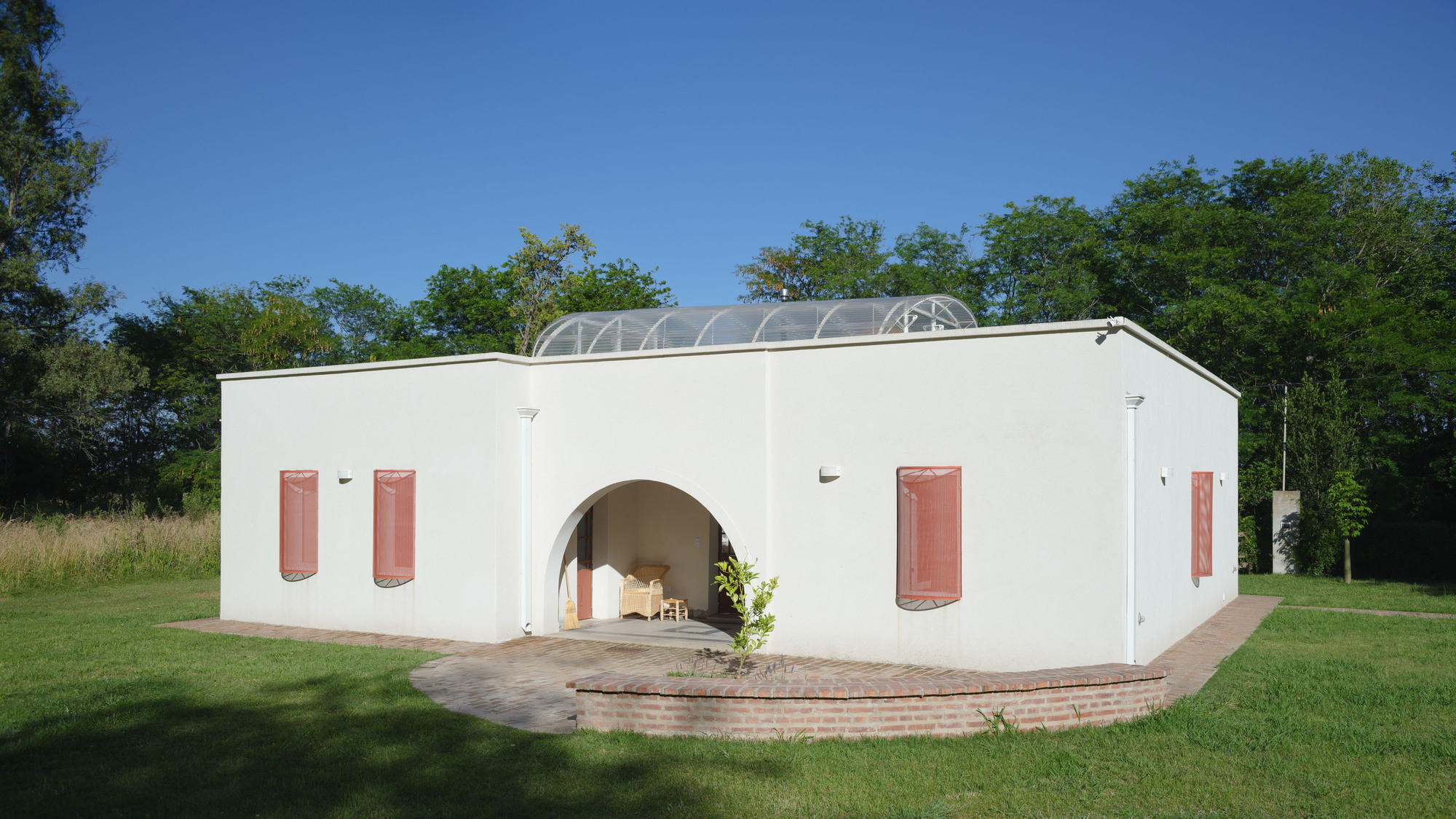 White stucco facade with terracotta shutters and central arched opening beneath a vaulted glass roof