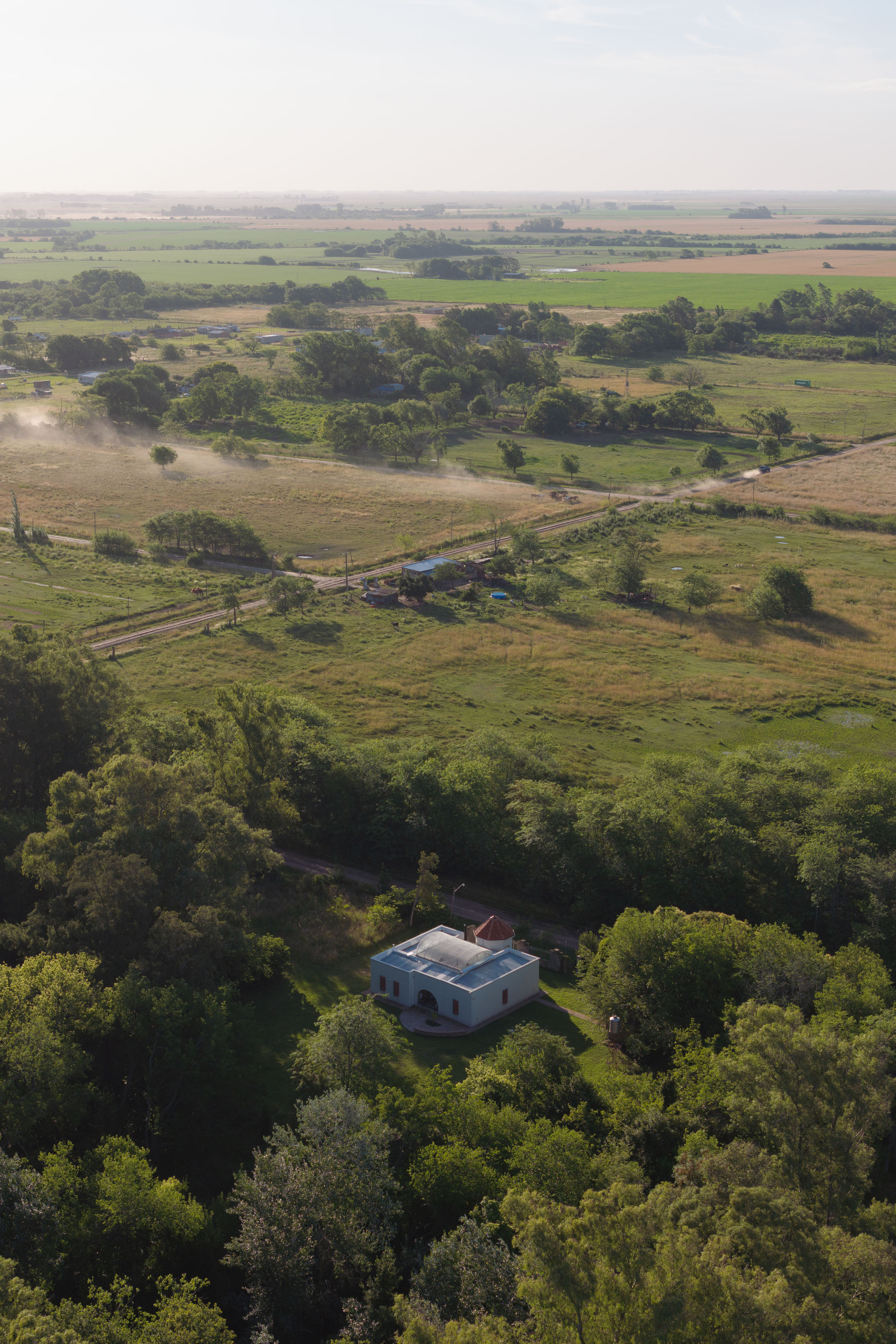 Aerial view of the white structure surrounded by dense tree canopy in agricultural landscape