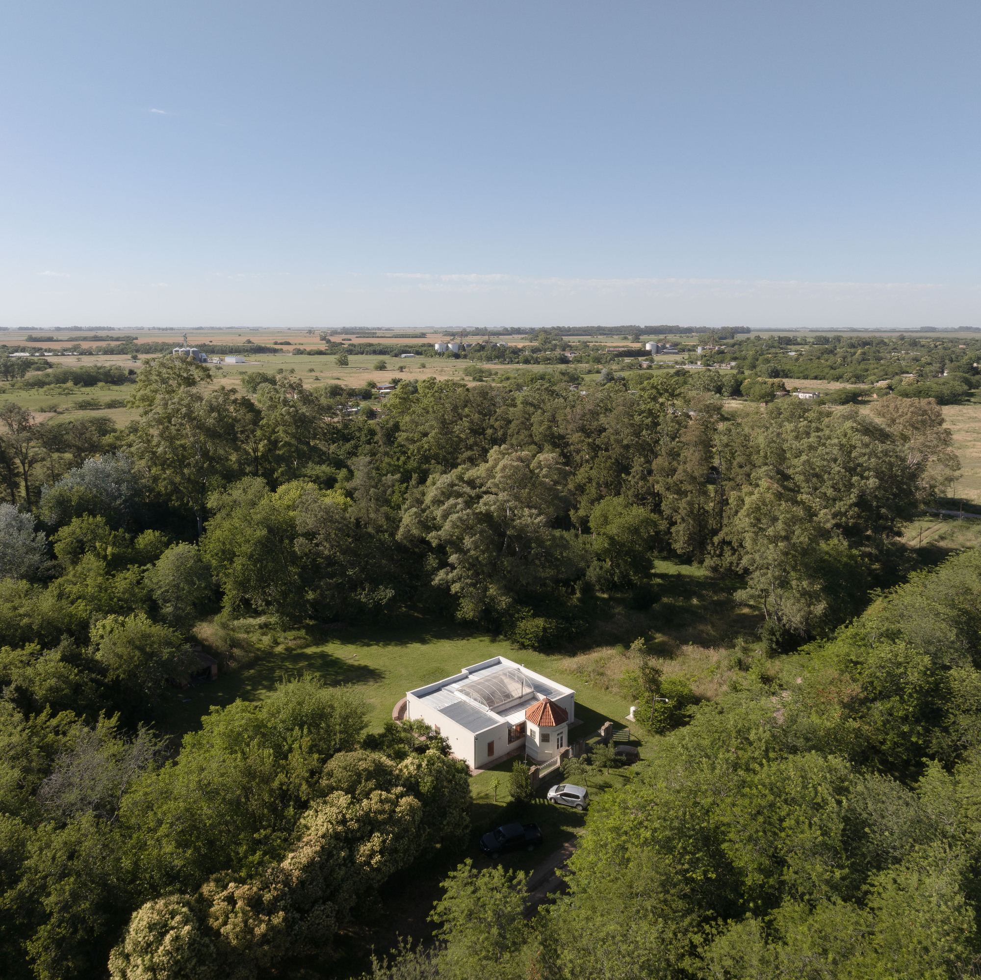 Drone perspective showing the building nestled among trees with open farmland beyond