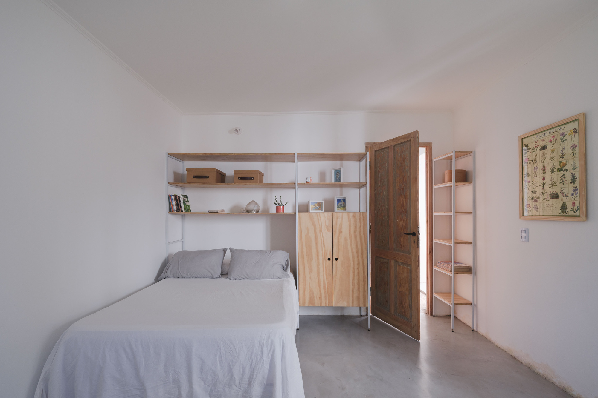 Bedroom with concrete floor, timber cabinetry and light shelving framing the bed