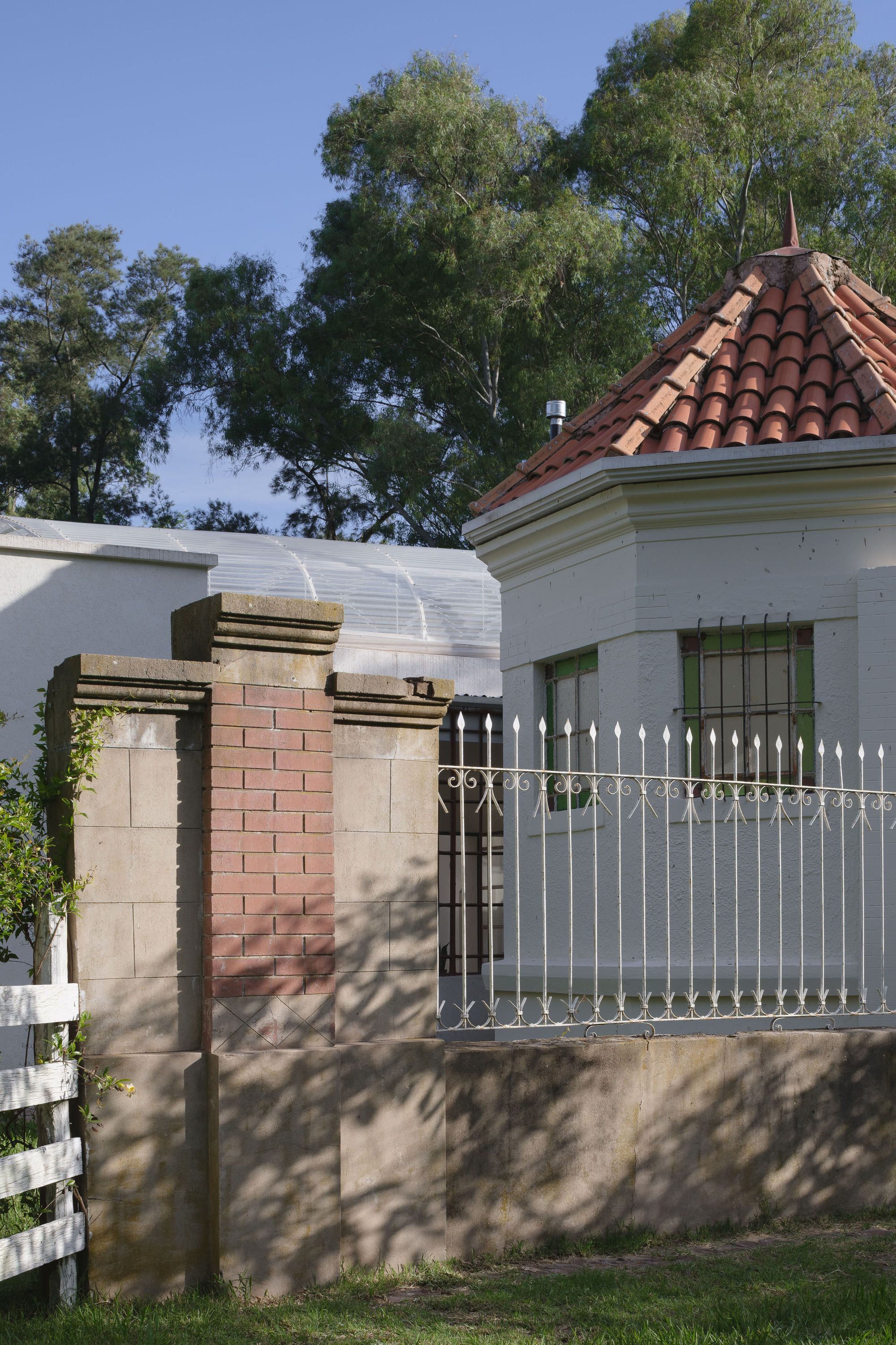 Street view of the residence showing terracotta dome roof, corrugated metal addition and masonry gateposts under trees