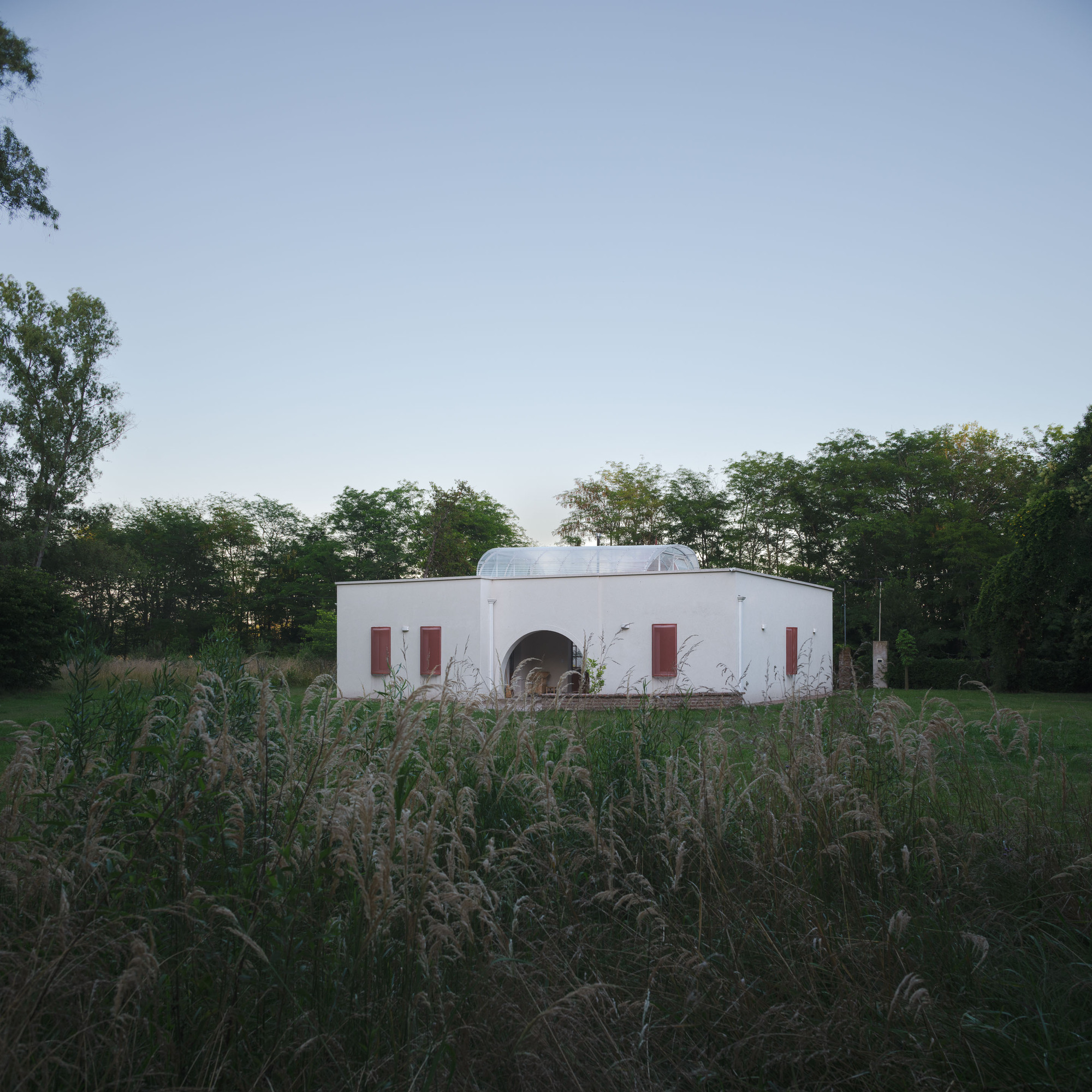 White stucco pavilion with arched entry and domed roof set in an open meadow of tall grasses