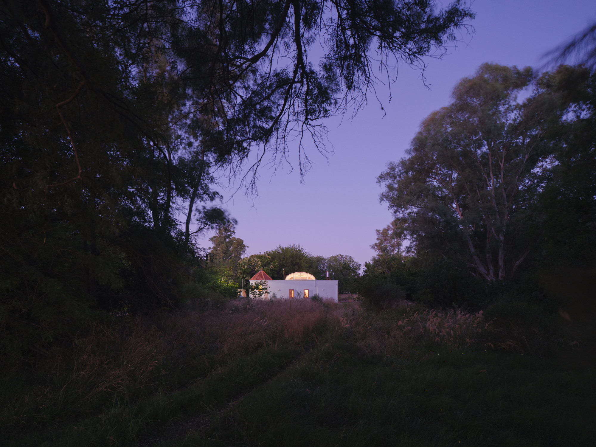 Distant view of the illuminated structure across wild grassland at dusk under purple sky