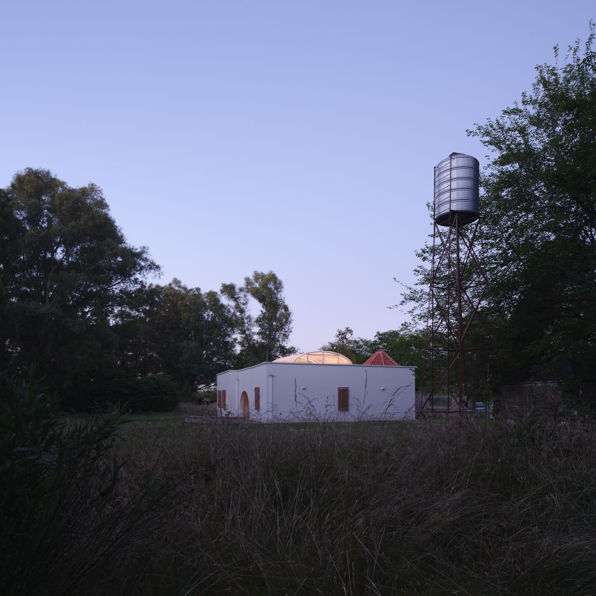 Rear elevation showing the domed volumes and adjacent metal water tower at twilight