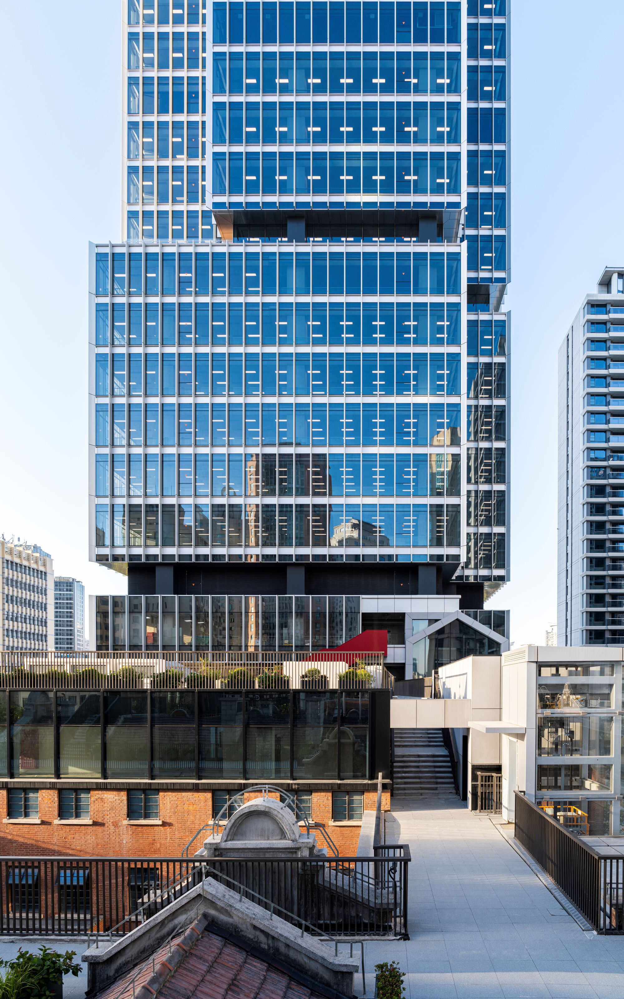 Blue glazed facade with projecting floor plates viewed from rooftop terrace at dusk
