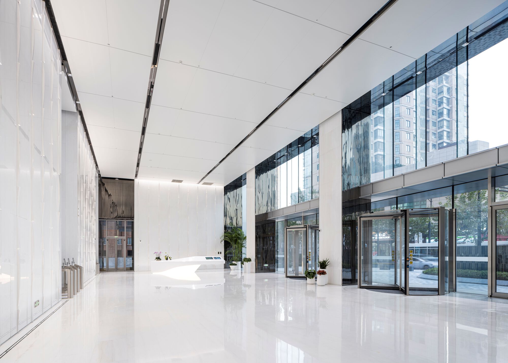 White polished floor lobby with full-height glazing and dark framed glass doors reflecting daylight