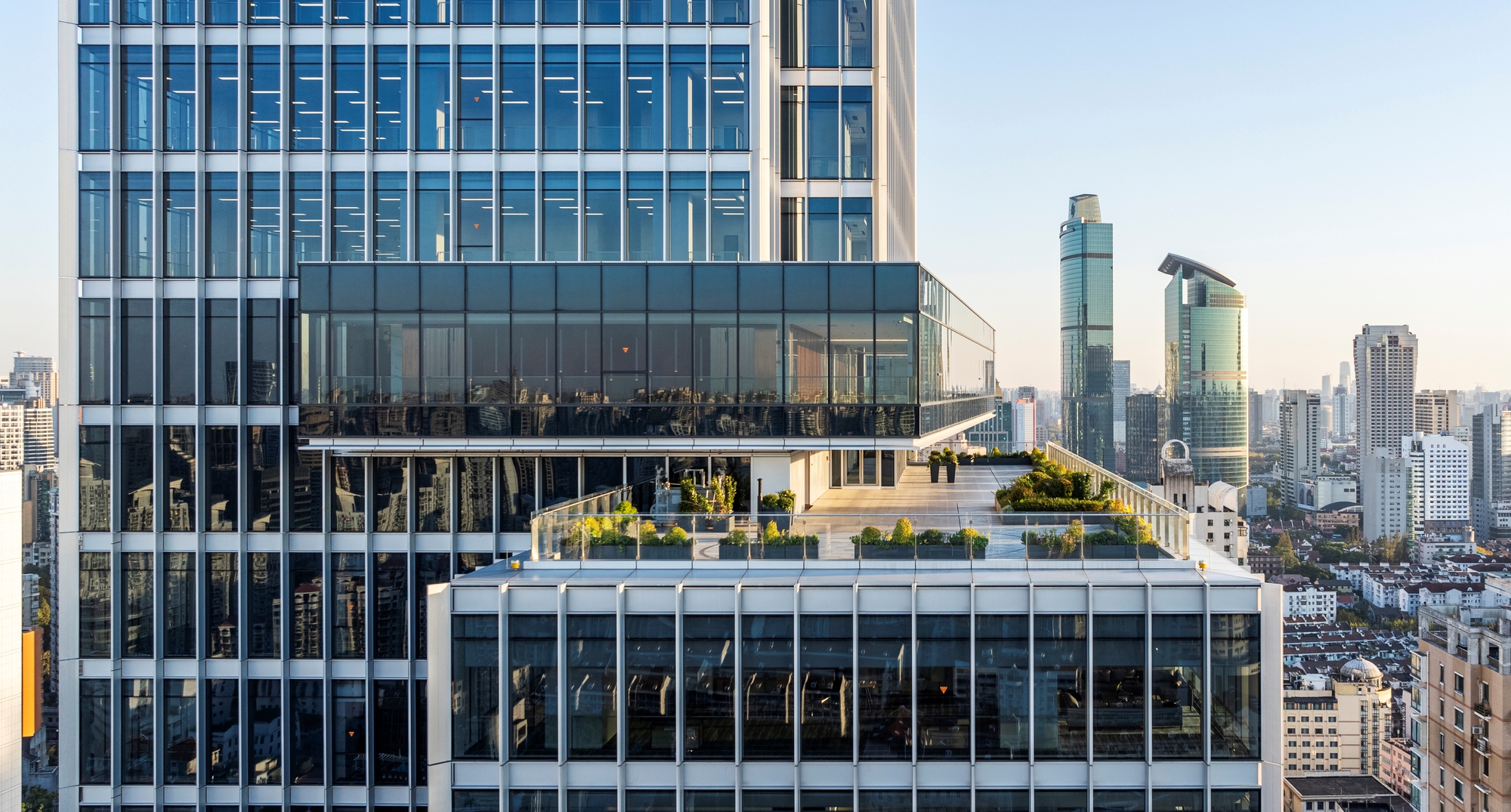Stacked terraces with glass balustrades and planted edges overlooking the skyline at dusk