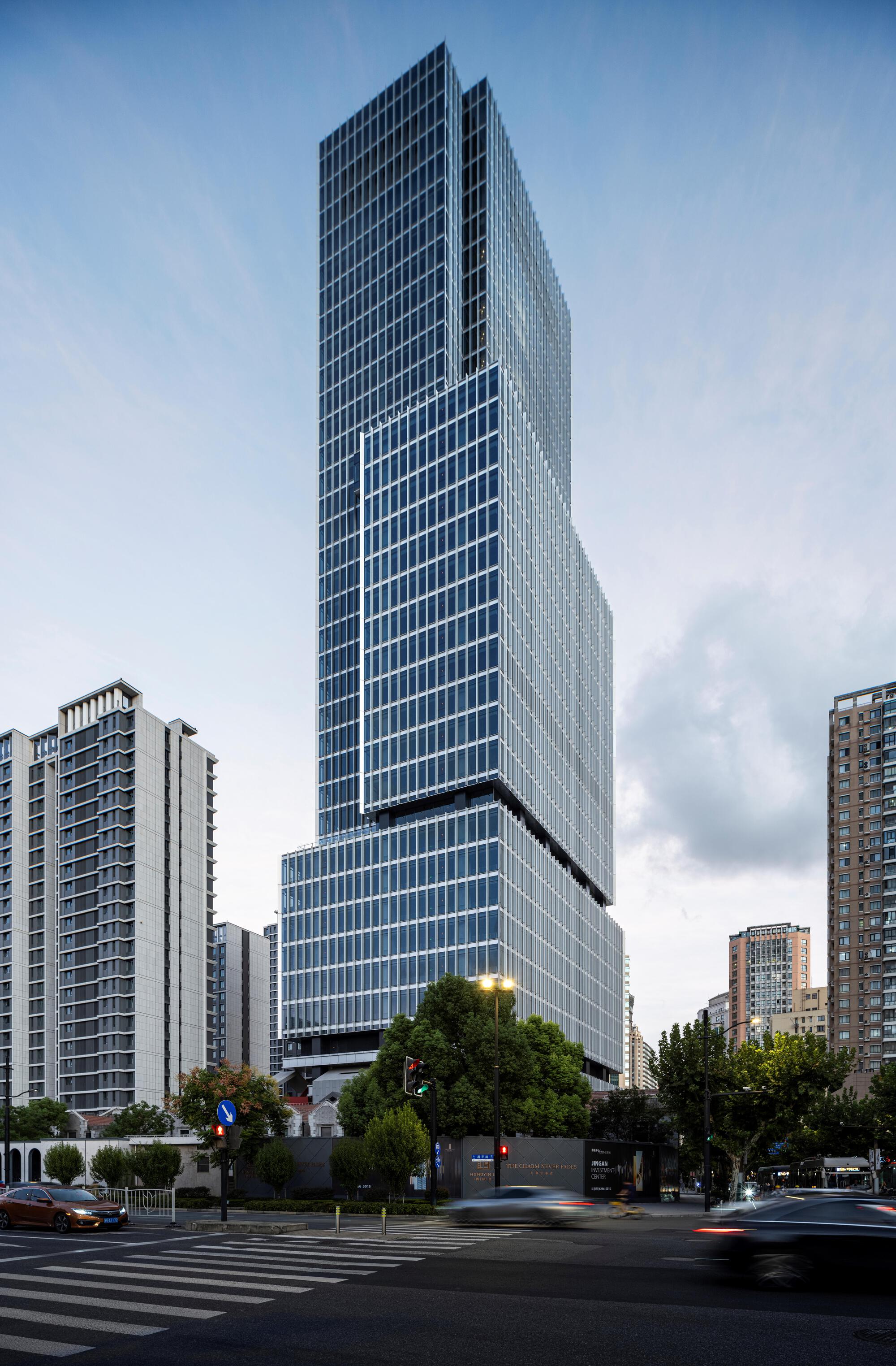 Cantilevered glass tower volume above the podium base with trees lining the street below