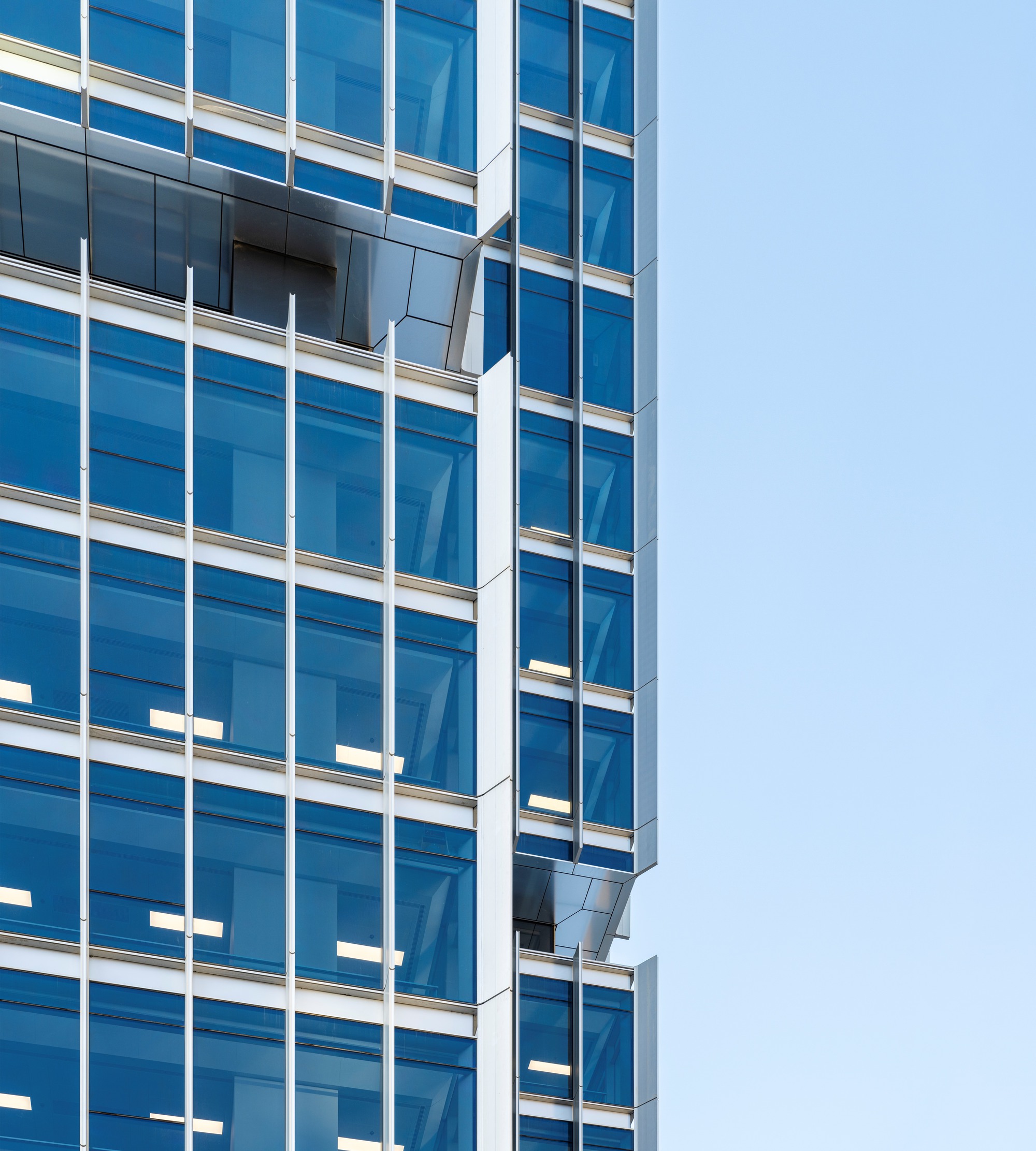 Detail of the blue glass curtain wall with white mullions and protruding balconies against a clear sky