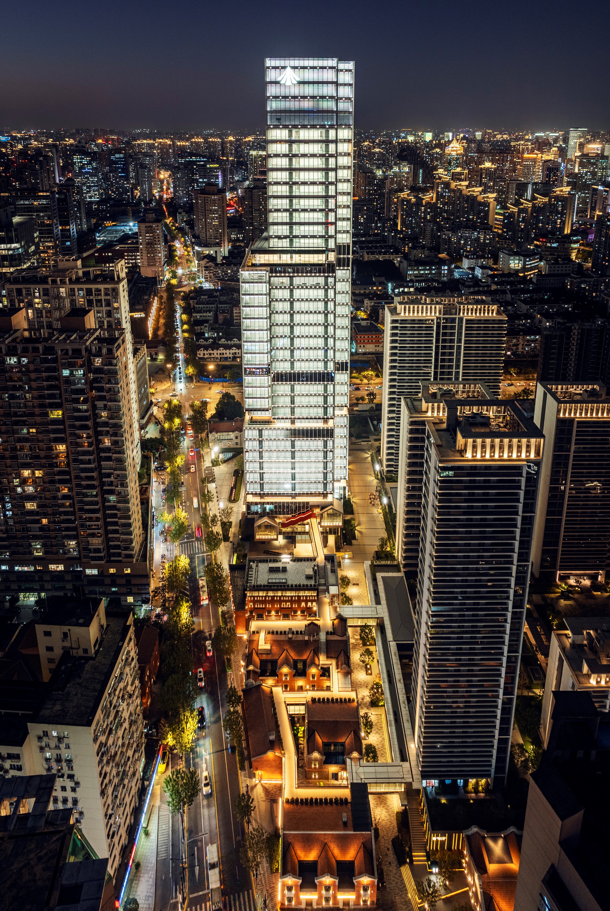 Aerial night view of the illuminated glass tower rising above surrounding buildings and streets