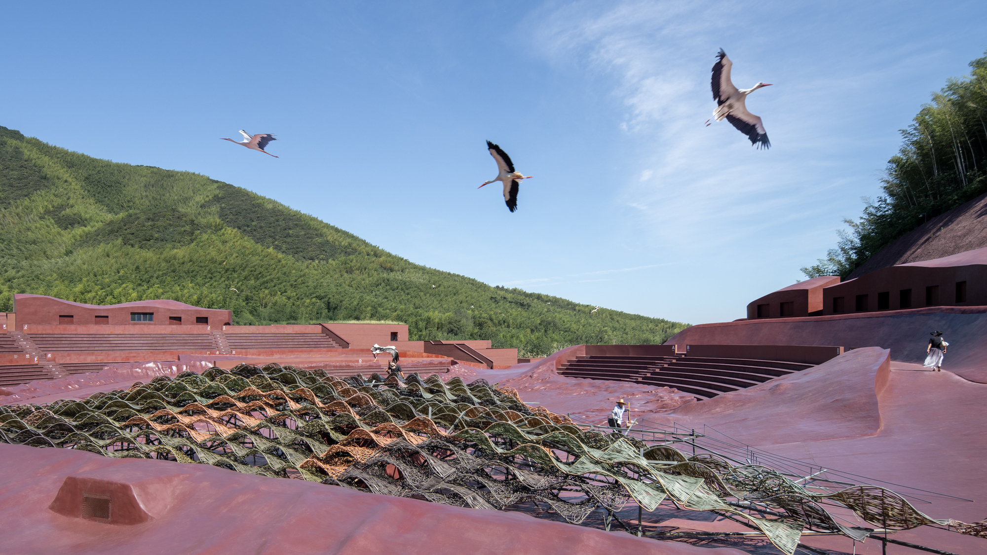 Amphitheatre seating and planted terraces with three cranes flying overhead in blue sky