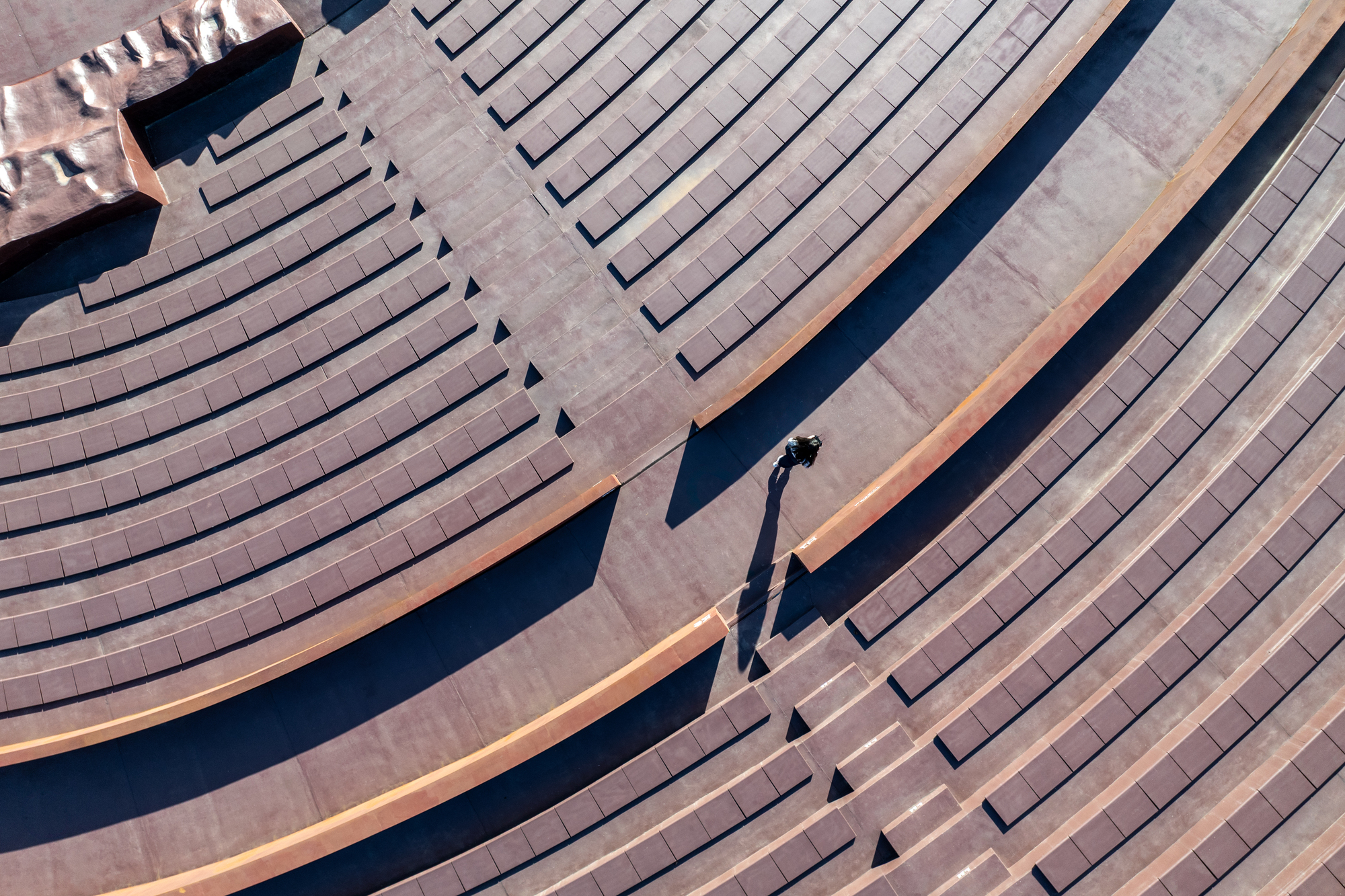 Aerial view of timber-clad terraced seating with a single figure casting long shadows