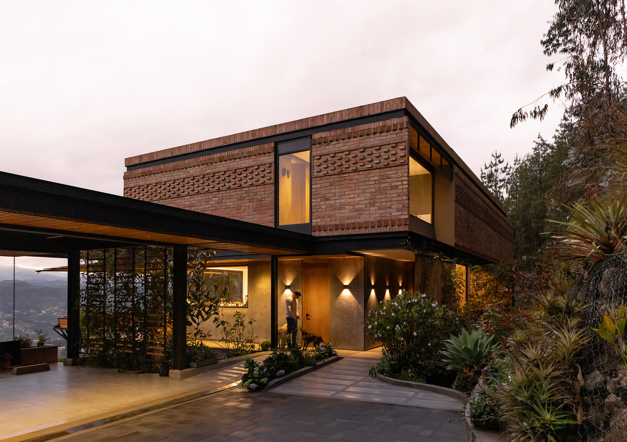 Two-story brick facade with patterned brickwork and entry court plantings at twilight