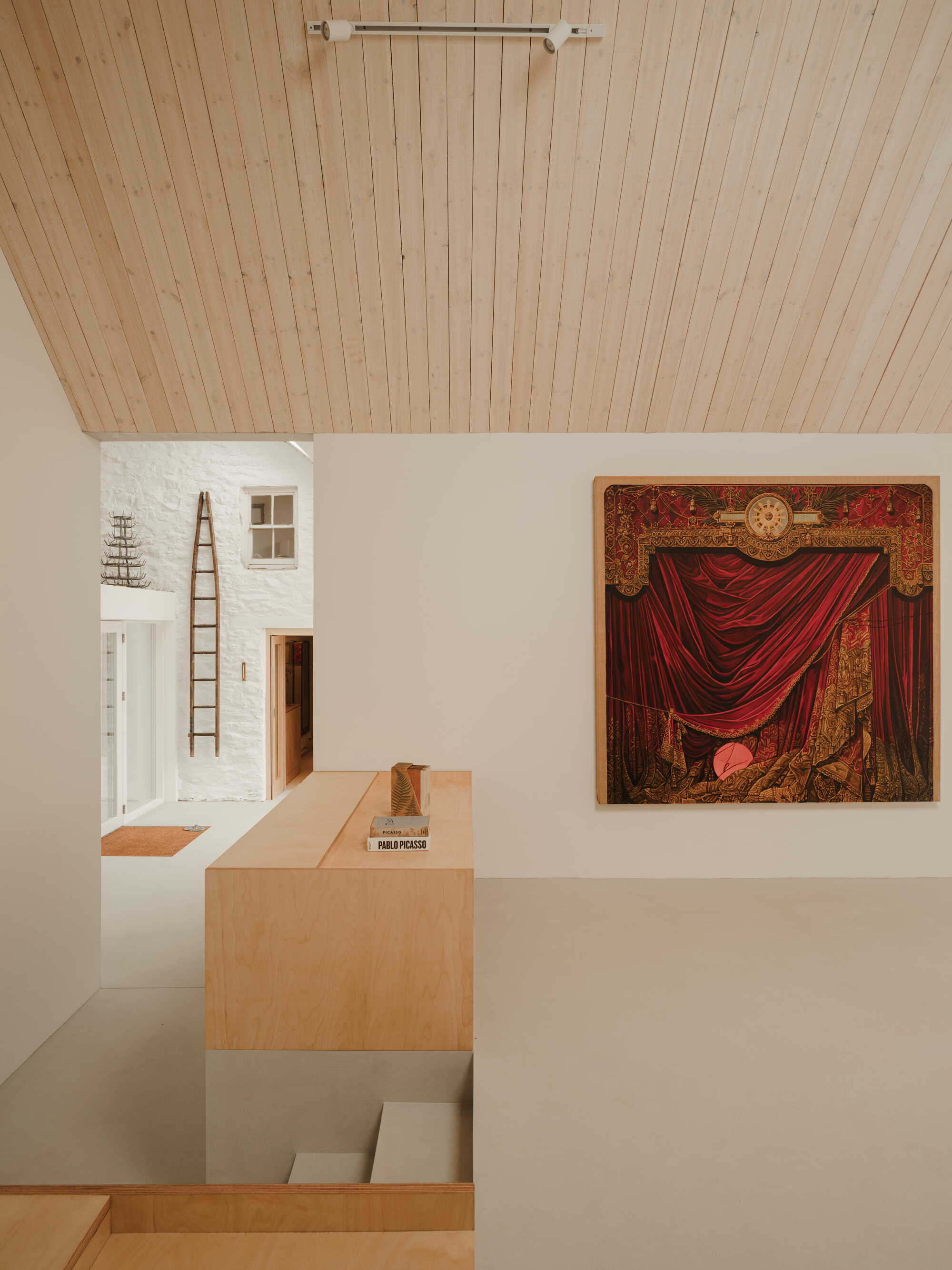 Interior view of a timber-lined vaulted ceiling above white walls displaying a red curtain painting