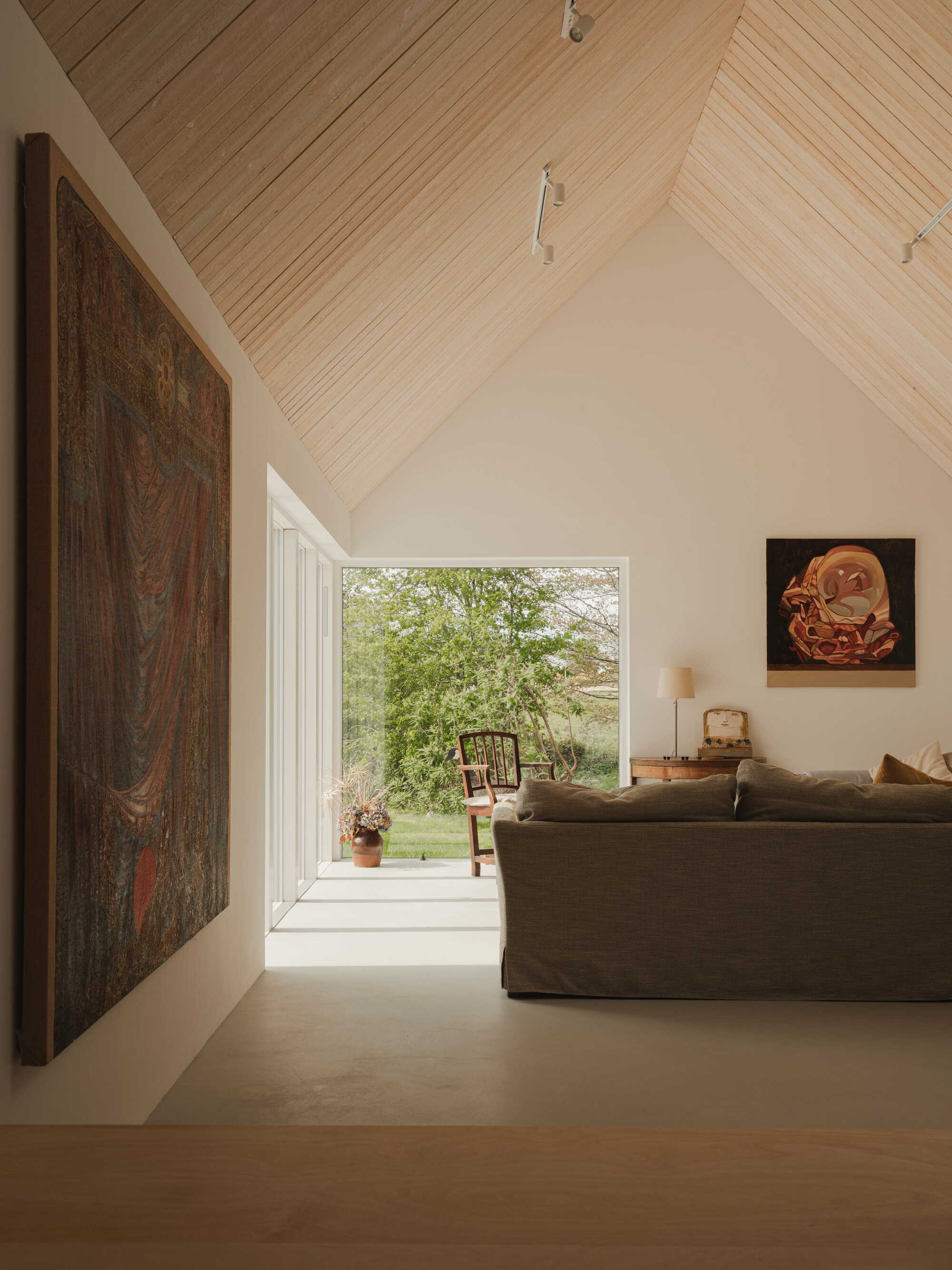 Living space with vaulted timber ceiling and full-height window framing a view of green trees outside