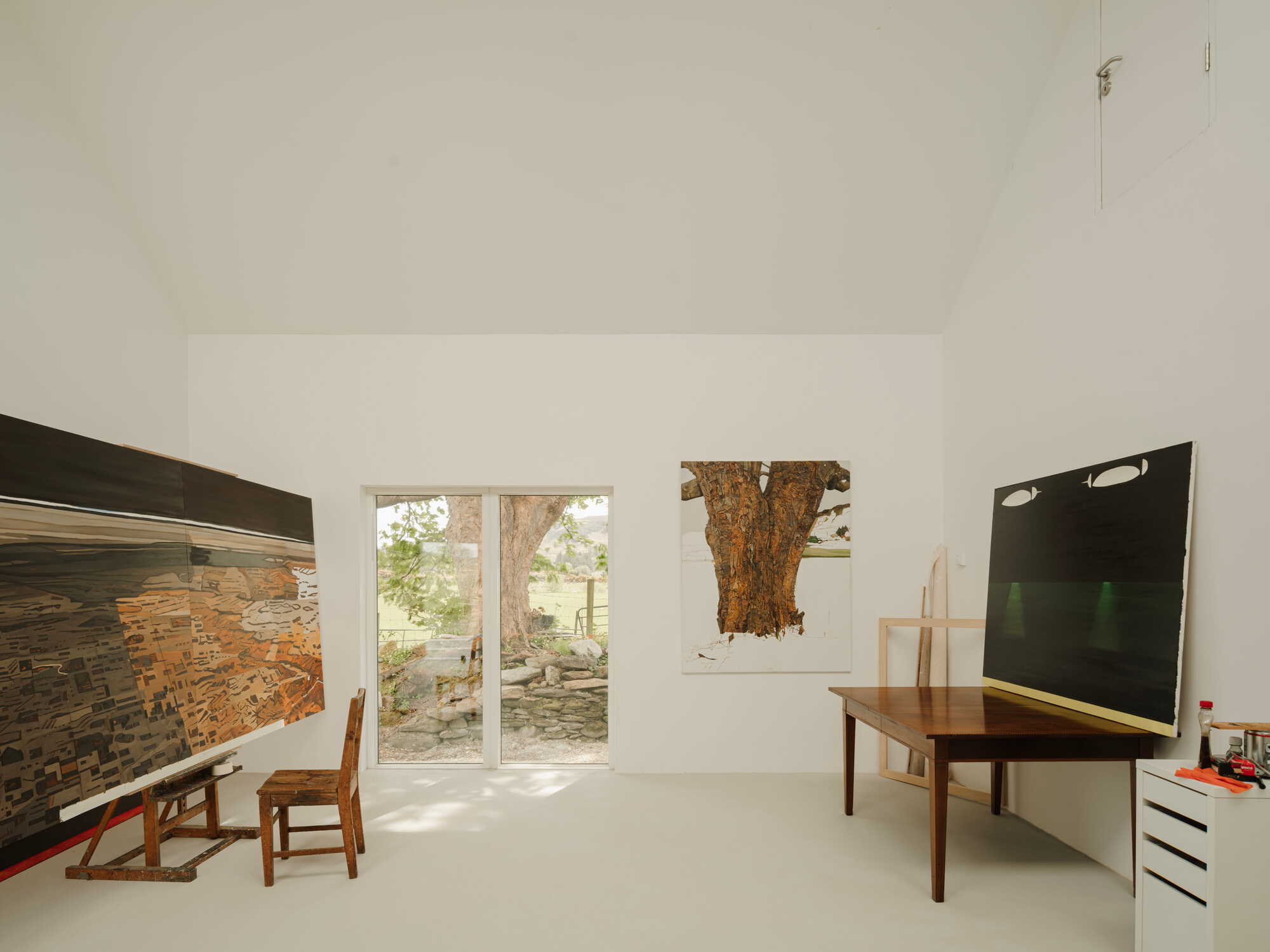 White-walled studio space with glazed doors opening to a stone wall and sunlit garden beyond