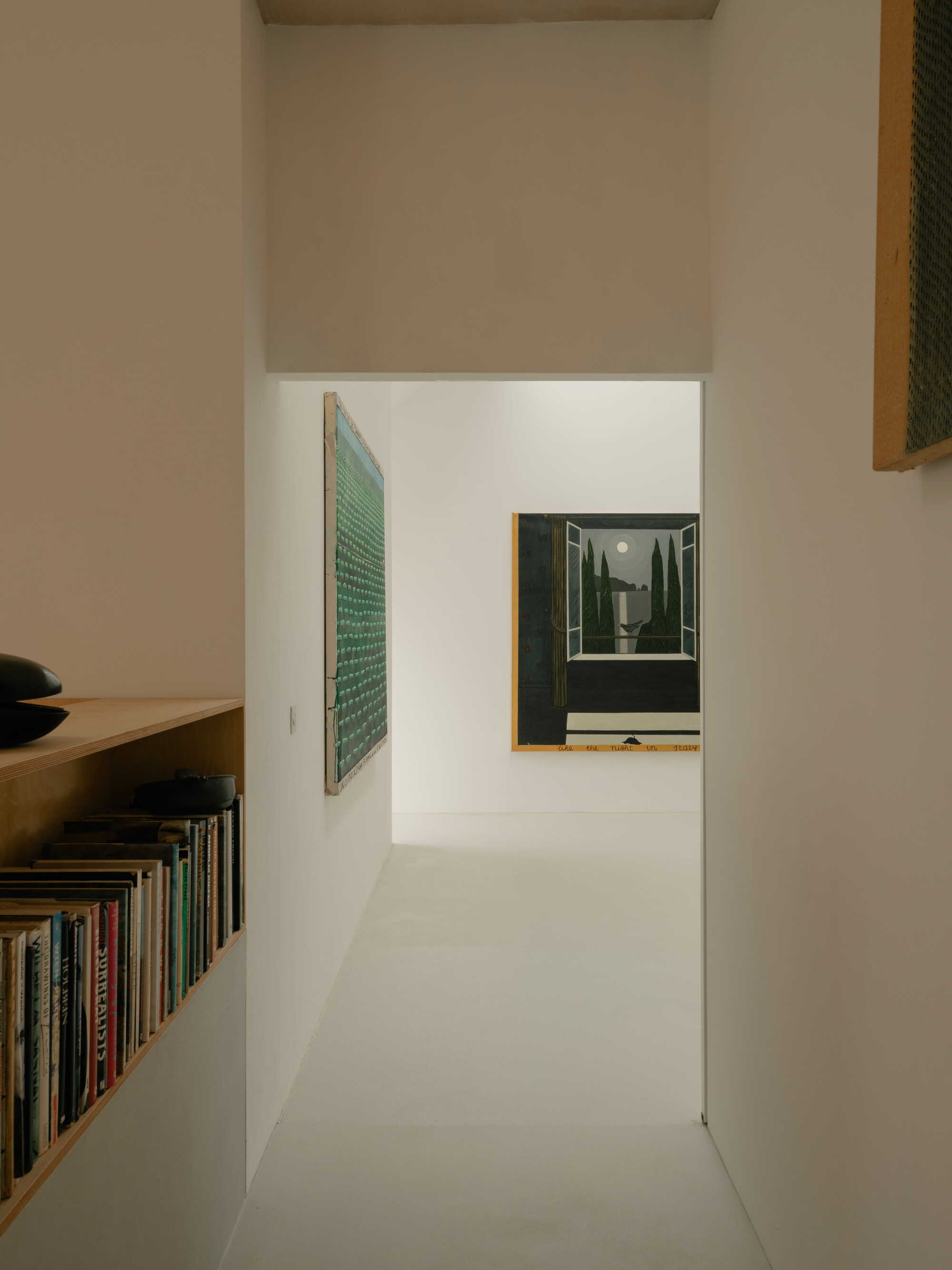 Narrow corridor with built-in plywood bookshelf and framed artwork hanging on the white wall